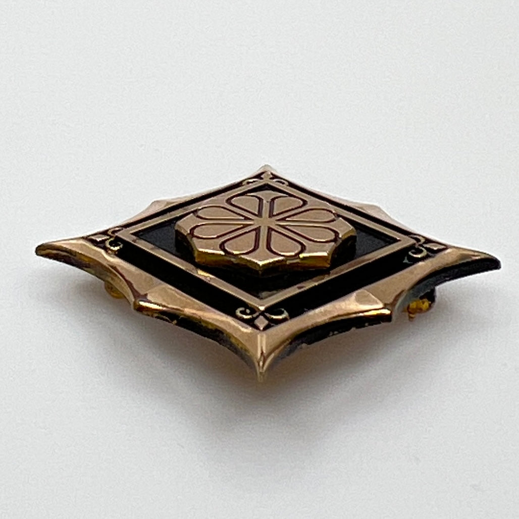 Angled view of cTo enamel brooch with raised medallion and deco-style edges