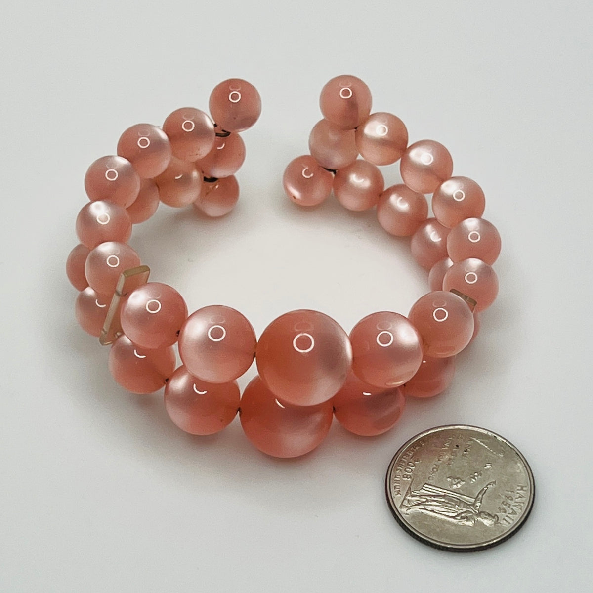 Pink beaded bracelet next to a quarter on a white background