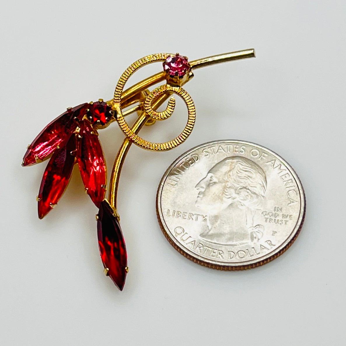 Vintage pink floral brooch next to a quarter for scale