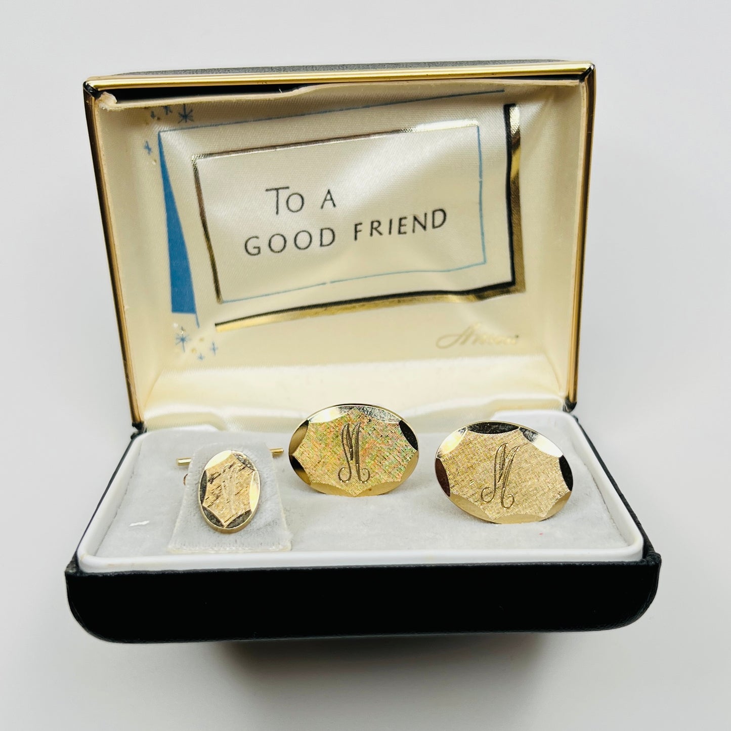 Gold cufflinks in a decorative box with 'To a Good Friend' message on a white background