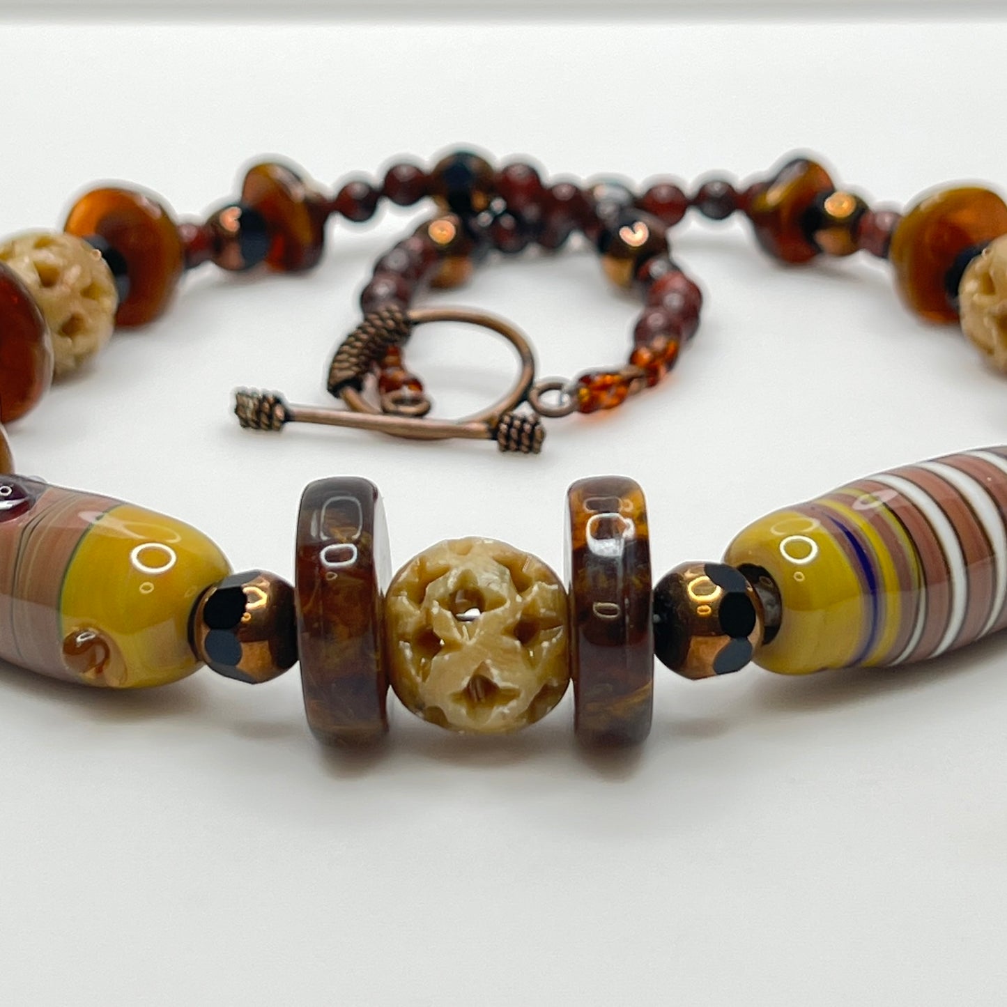 Close-up of striped glass beads, carved gemstone orbs, and copper clasp