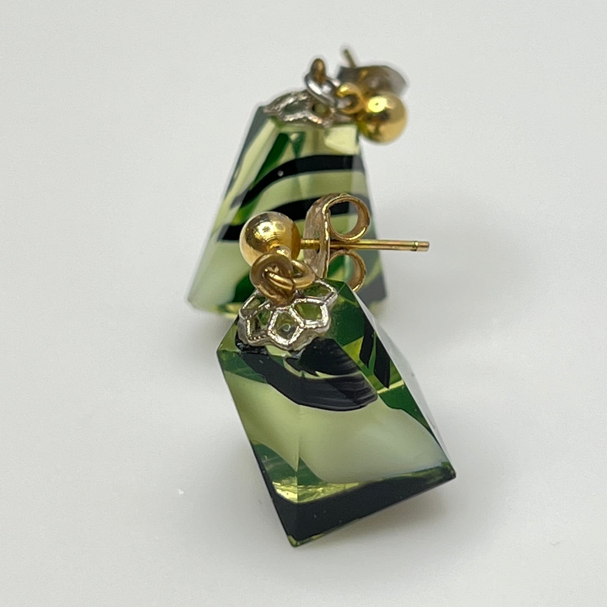 Green and black geometric earrings with gold accents on a white background