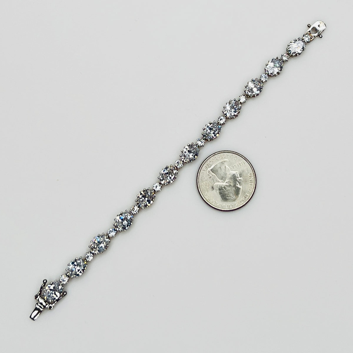 Full view of bracelet with alternating oval and round stones next to quarter for size comparison