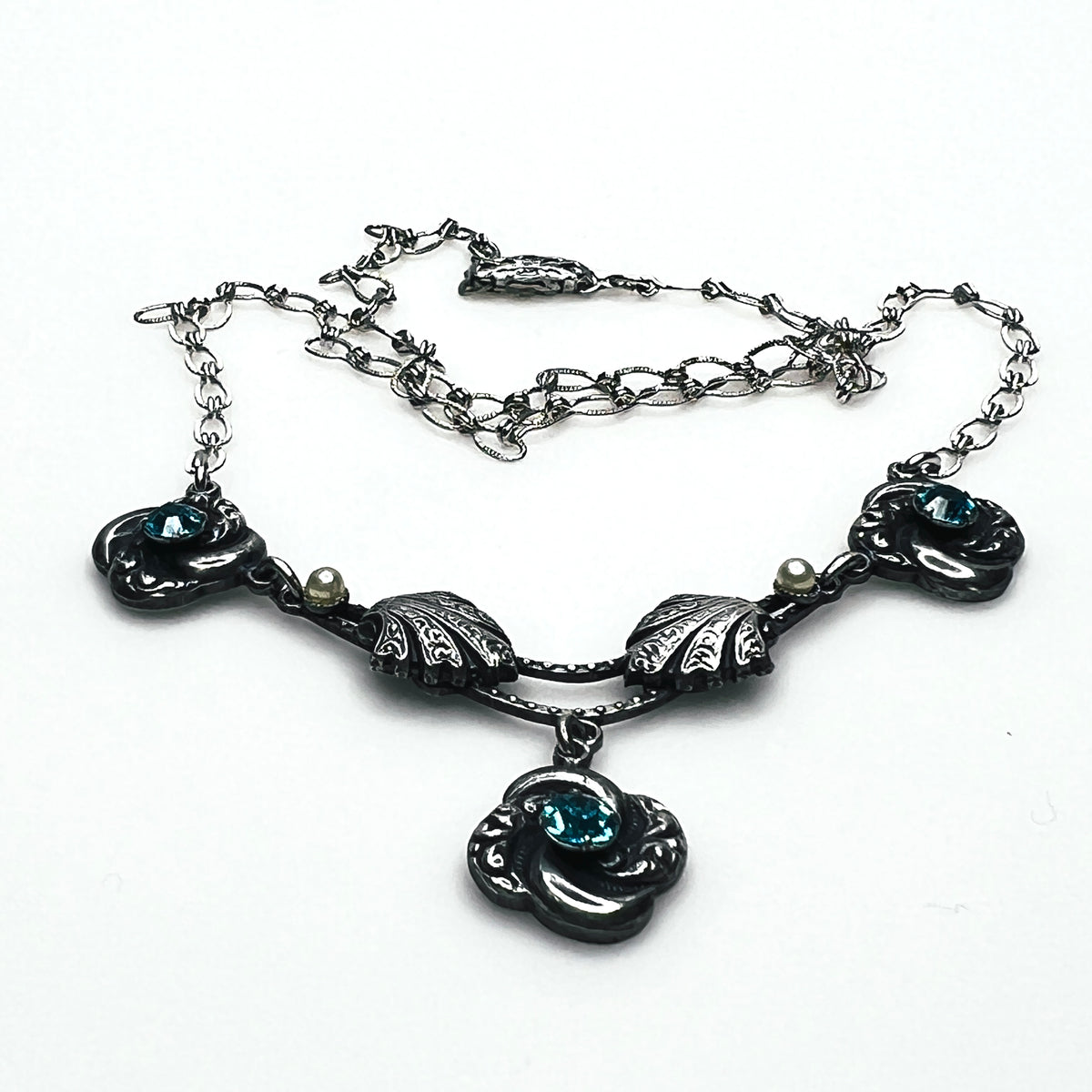 Side view of vintage silver-tone necklace showing dimensional floral ornaments, textured chain and central pendant.
