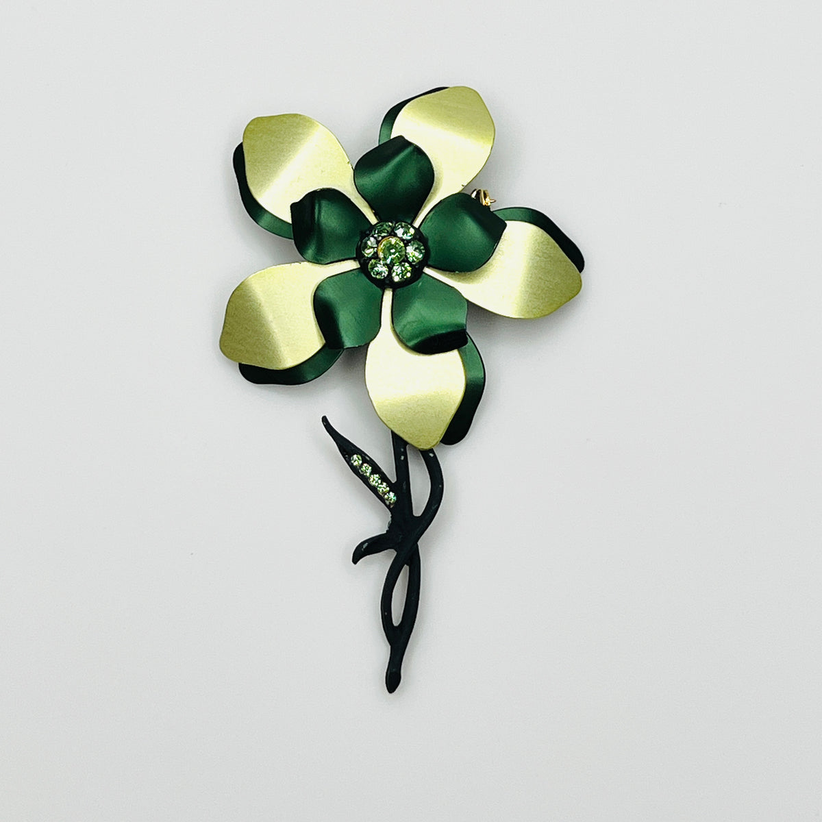 Vintage 1970s oversized green enamel flower brooch with layered emerald and chartreuse petals, green rhinestone center, and sculptural black stem.