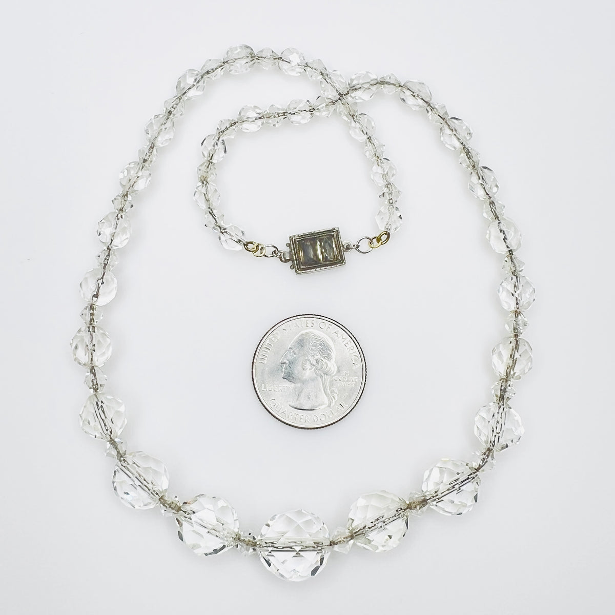 Vintage faceted crystal necklace beside quarter for scale