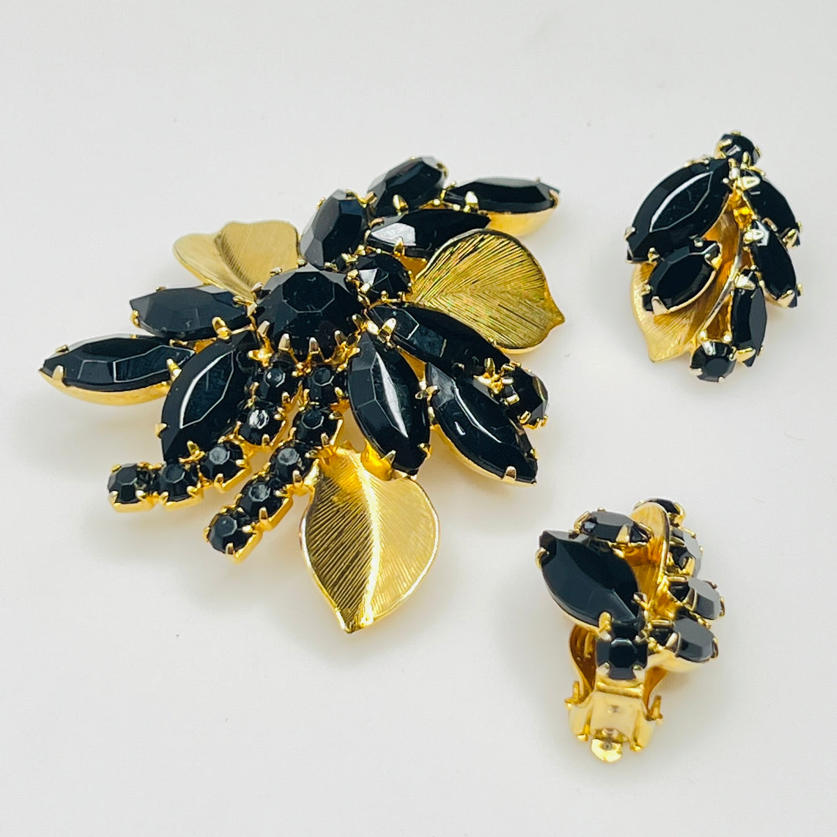 Close-up of Weiss signed black rhinestone clip-on earrings with gold leaf accents