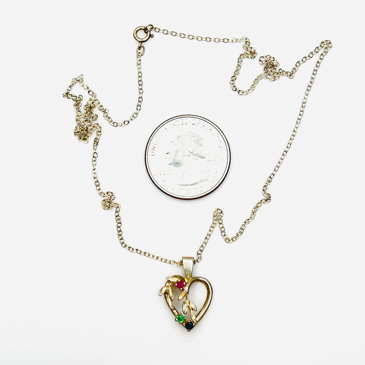 Vintage sterling silver heart pendant necklace beside quarter showing size and gemstone details.