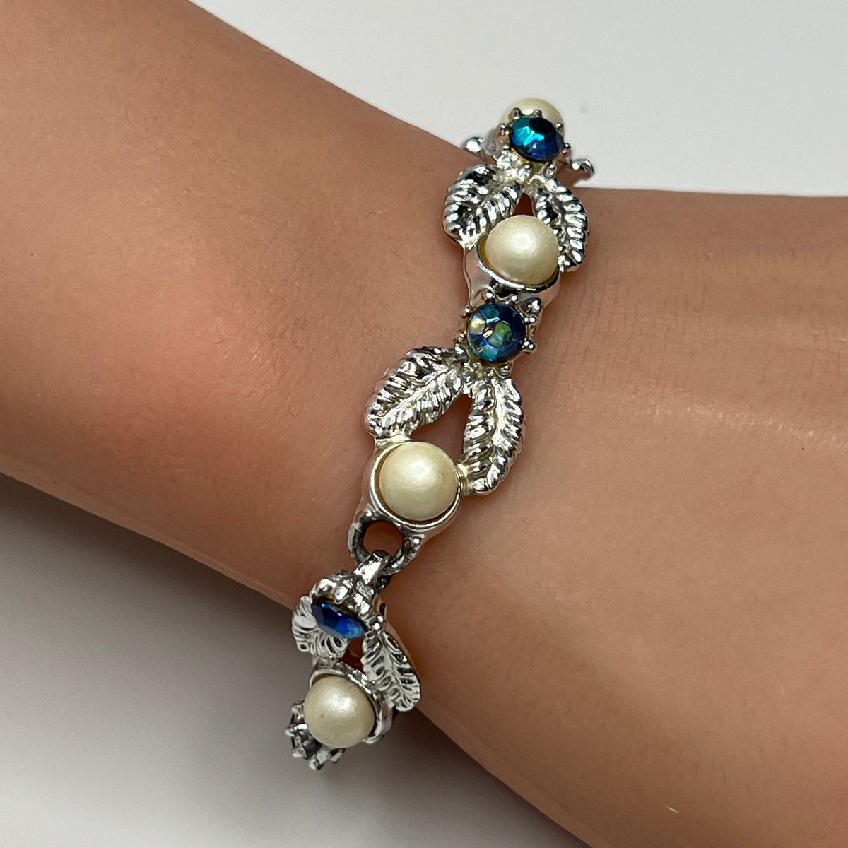 Silver leaf link bracelet with faux pearls and blue rhinestones worn on wrist