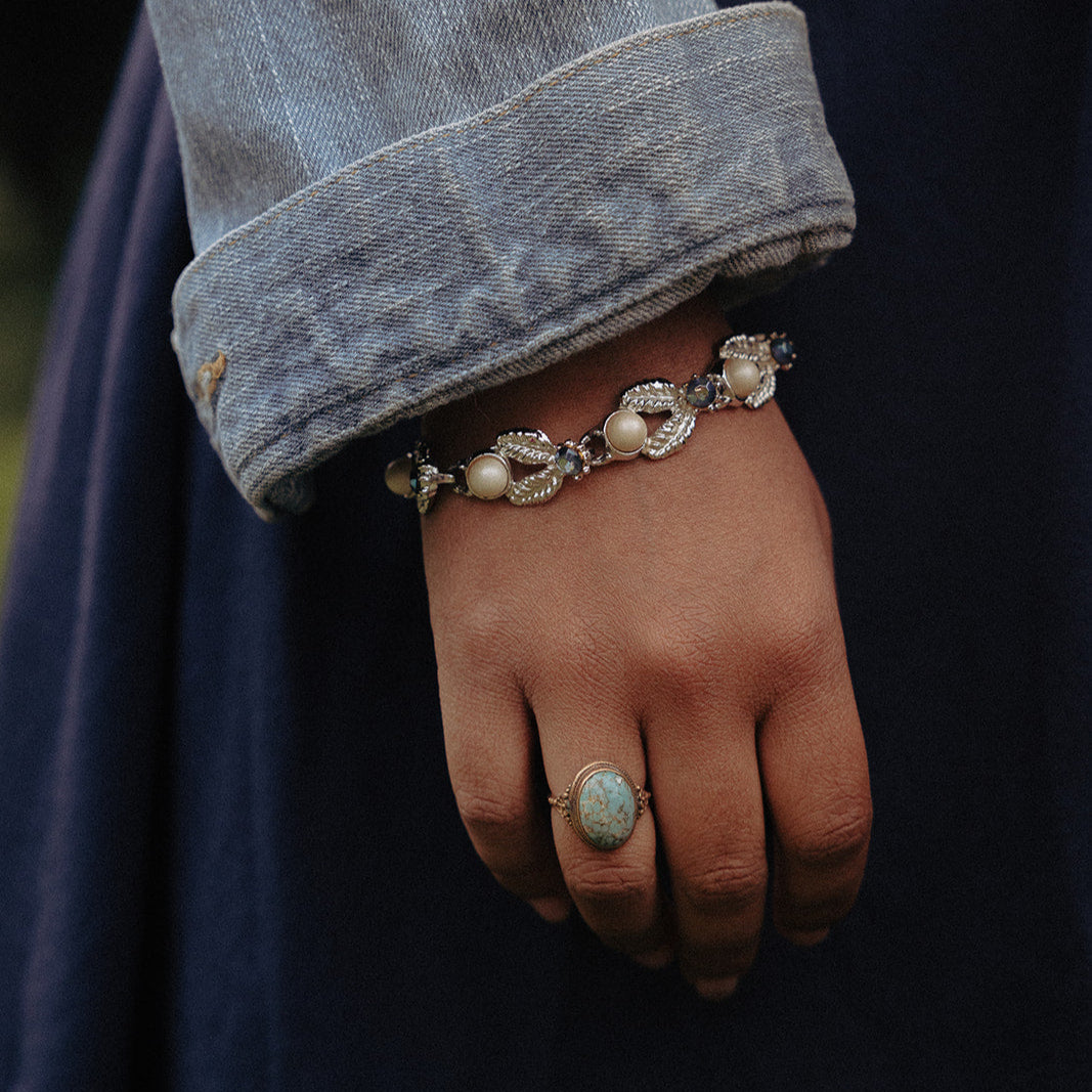 Silver leaf link bracelet with faux pearls and blue rhinestones worn on wrist