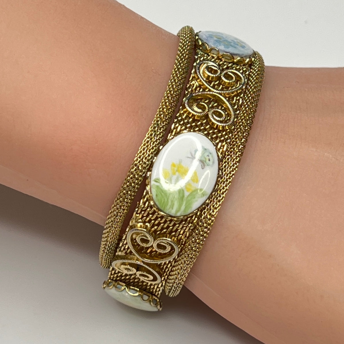 Gold mesh bracelet with hand-painted floral cabochons worn on wrist