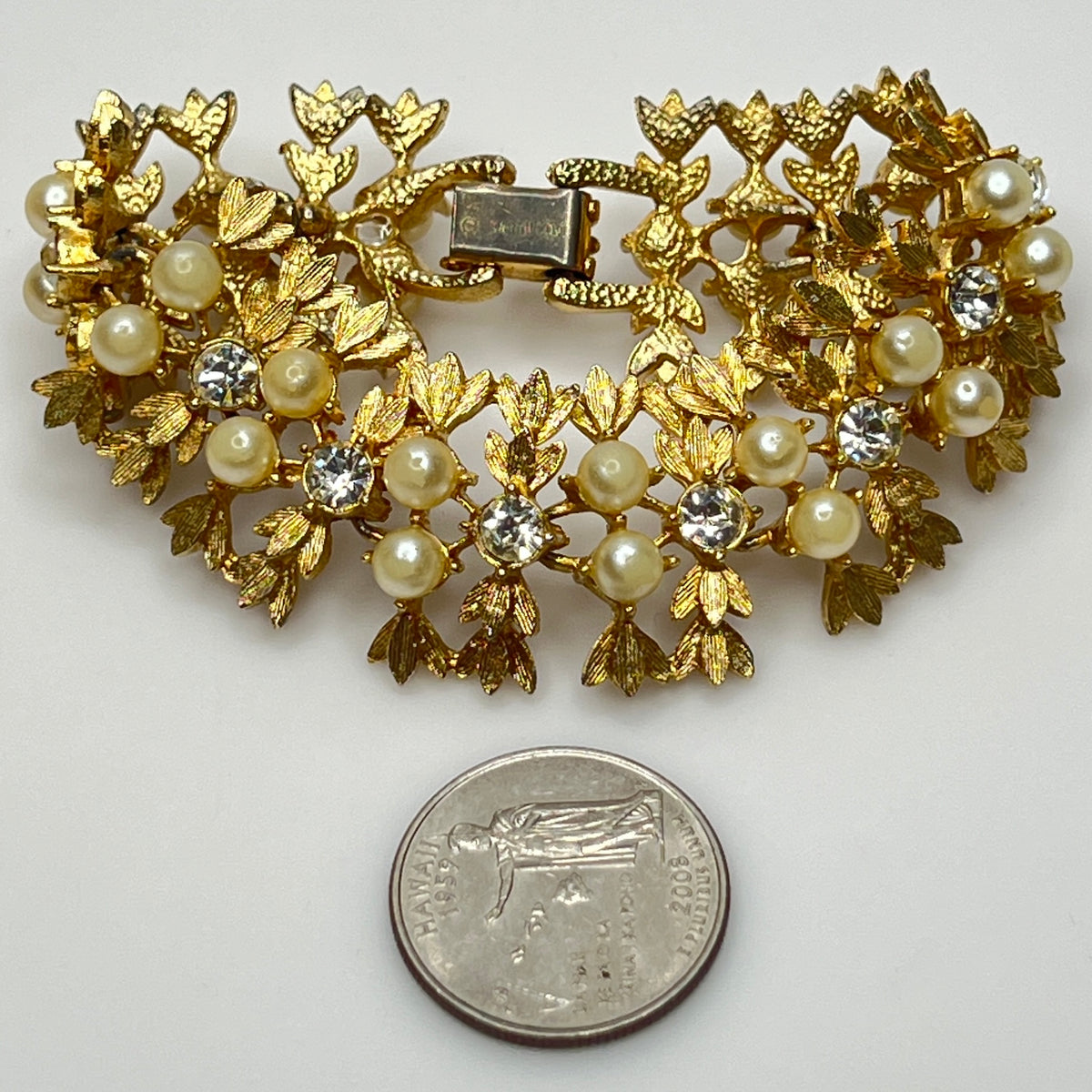 Gold brooch with pearls and crystals next to a quarter for scale on a white background