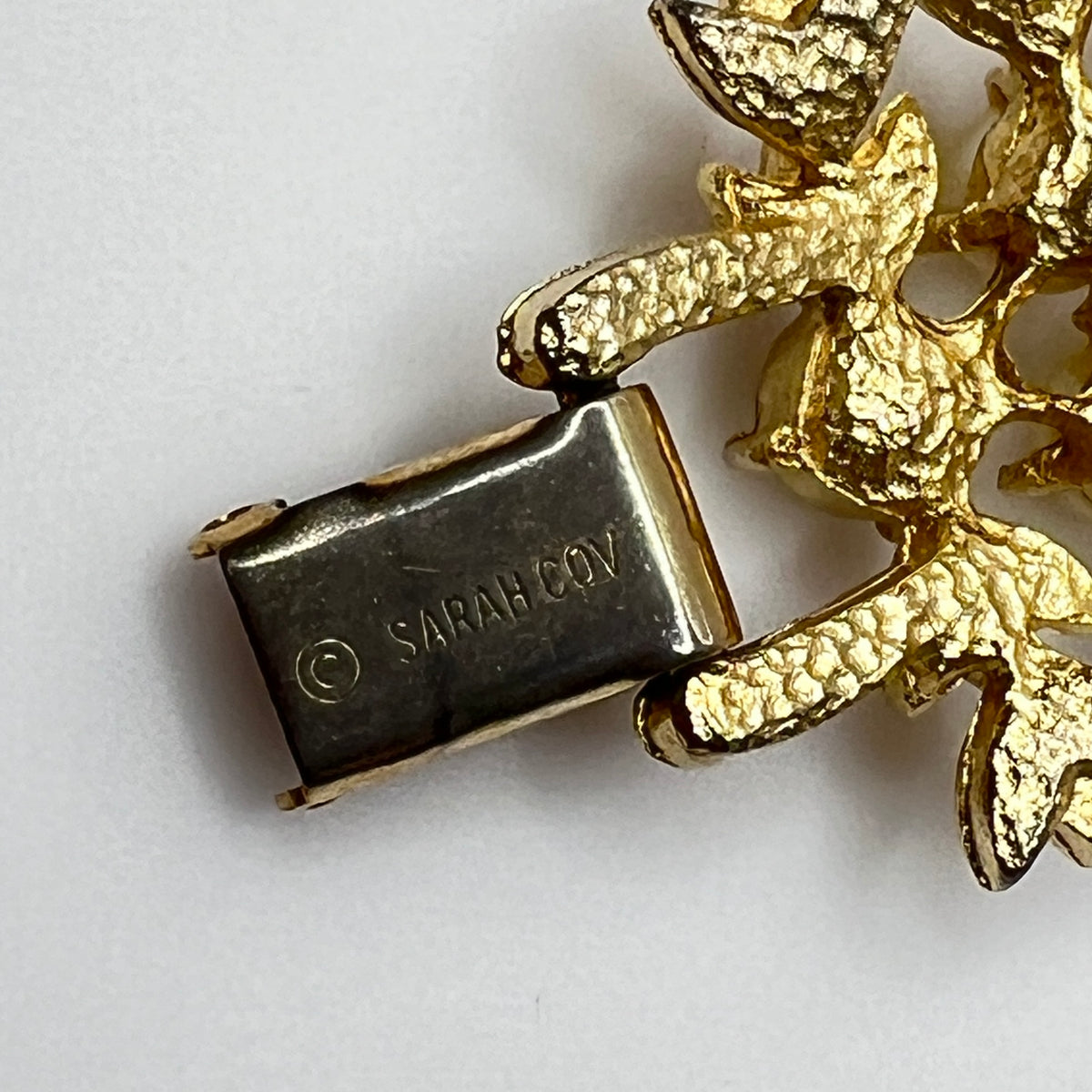 Gold bracelet with 'SARAH COV' clasp on a white background