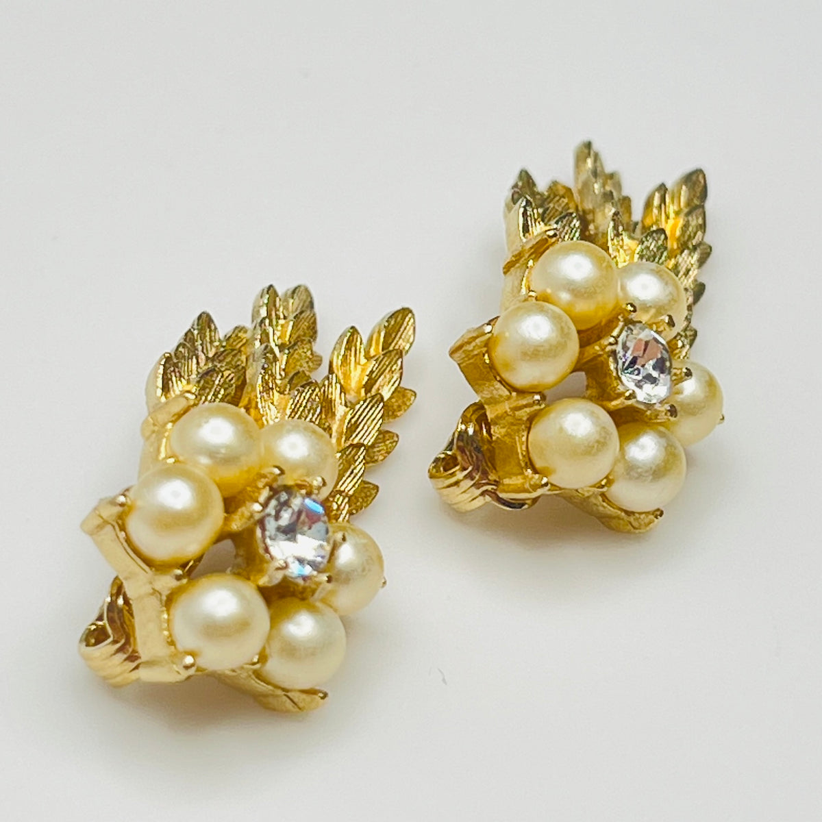Pair of gold earrings with pearls and clear stones on a light background