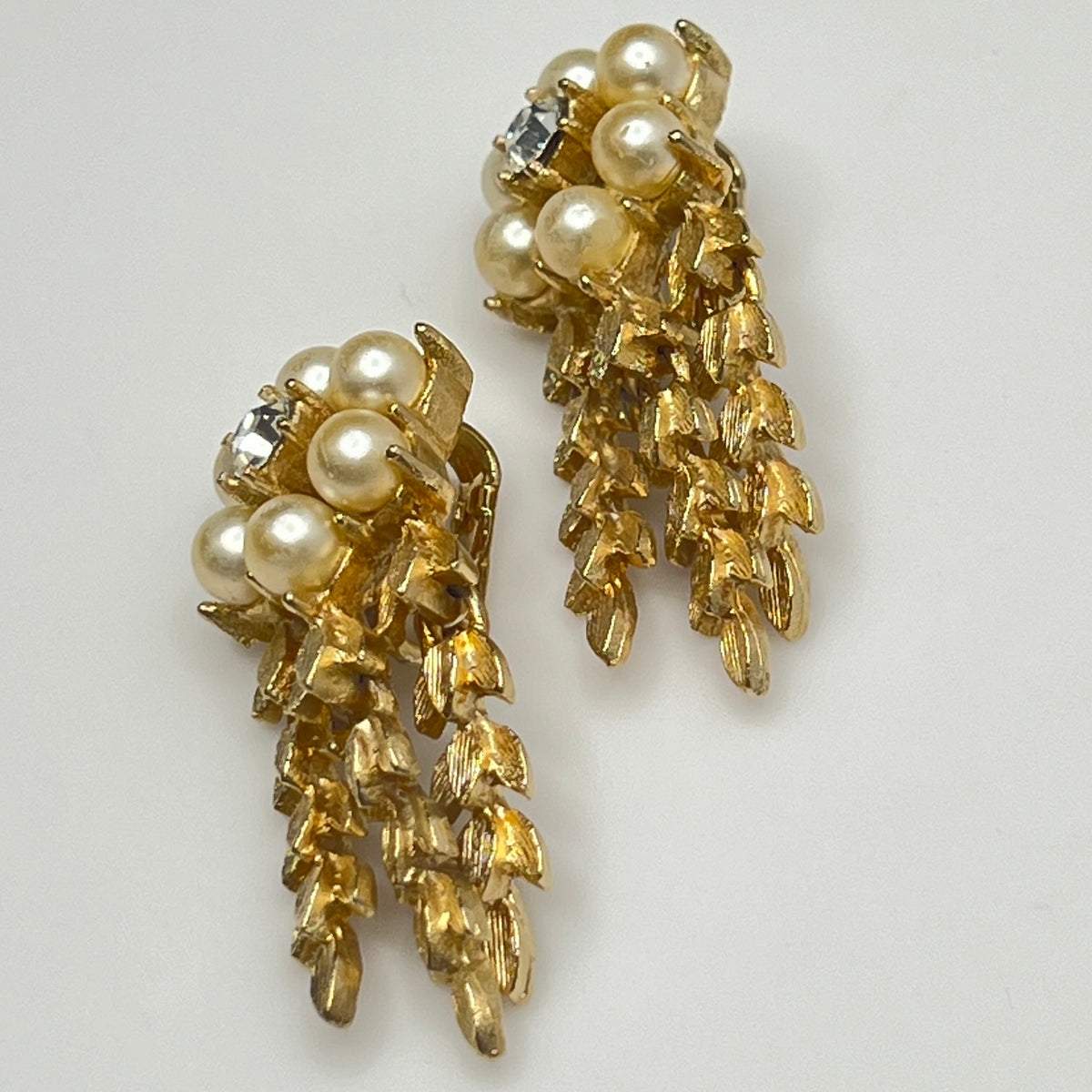 Gold earrings with pearl-like stones on a light gray background