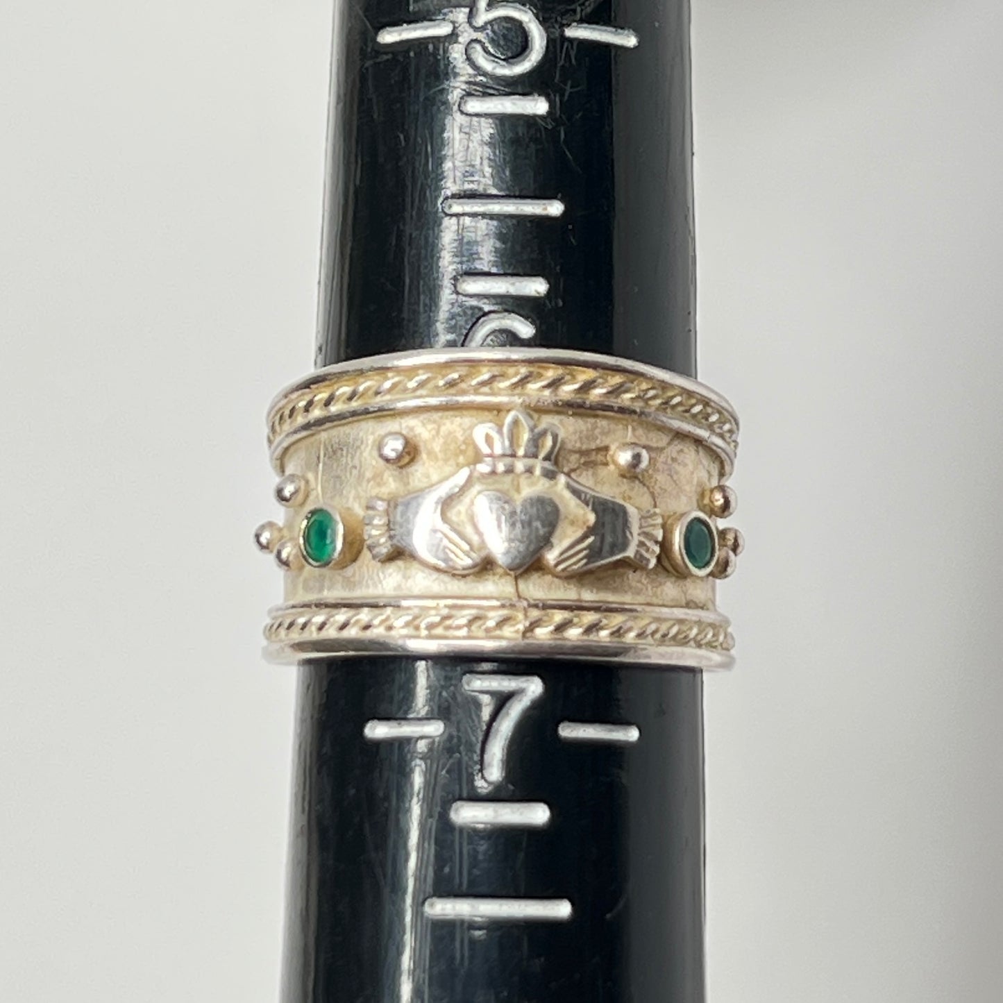 Close-up of Claddagh motif and emerald accent on wide silver ring