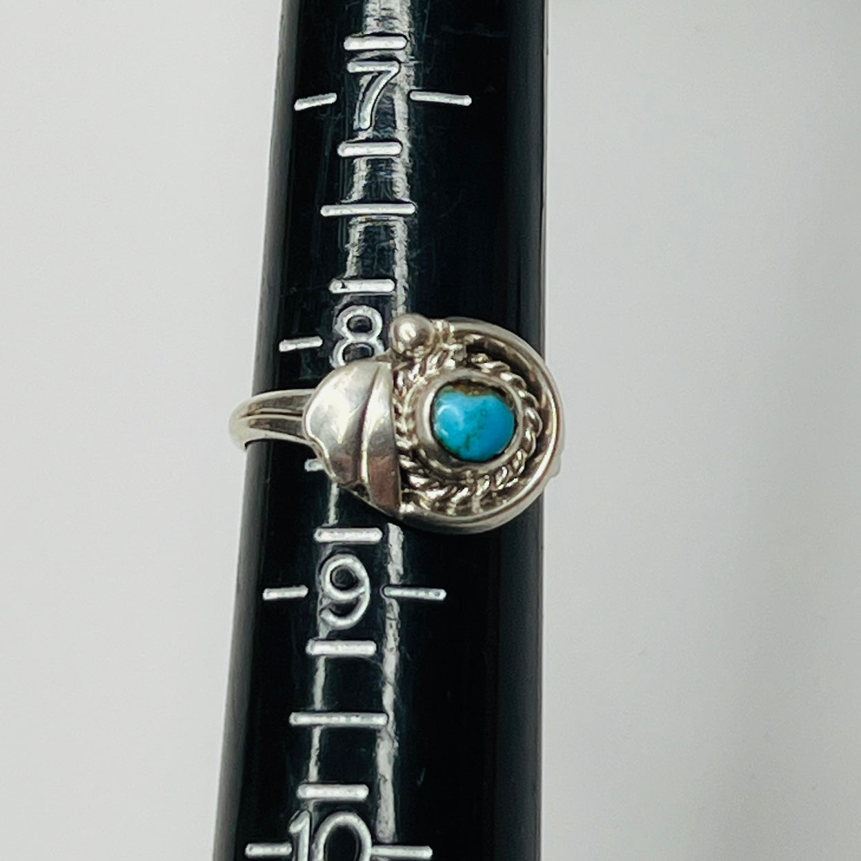 Close-up of turquoise ring showing rope and leaf motif on ring sizer
