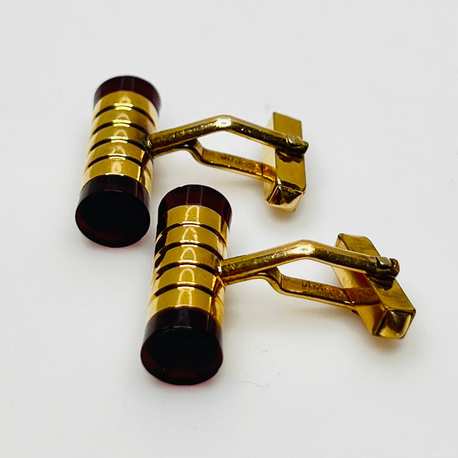 Close-up of cylindrical cufflinks with grooved goldtone design and red ends