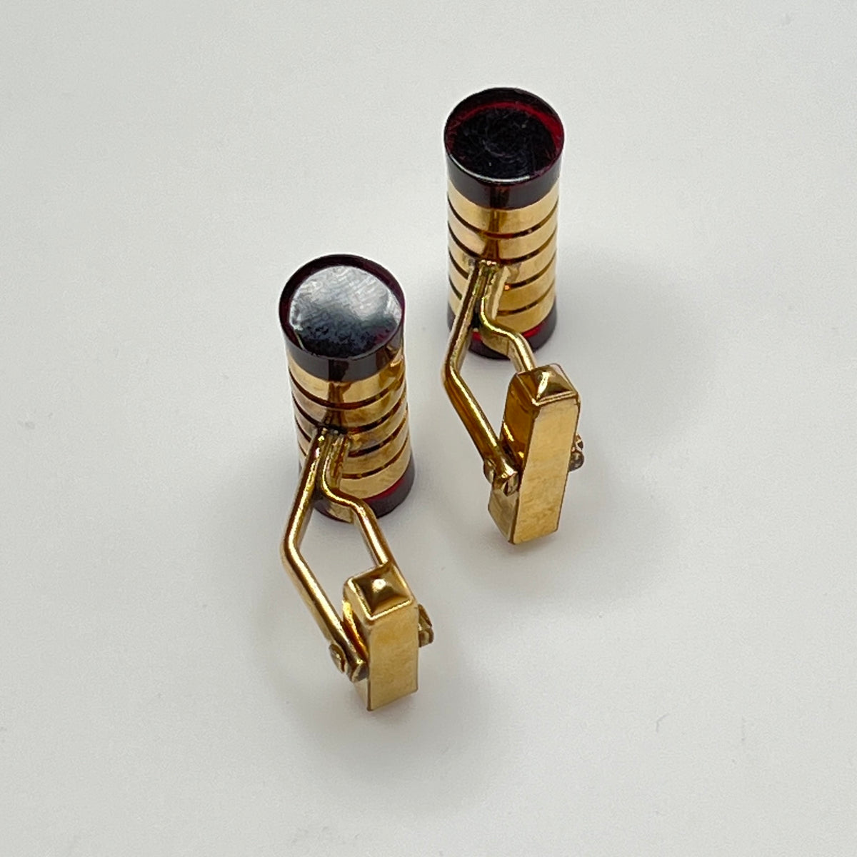 Close-up of cylindrical cufflinks with grooved goldtone design and red ends