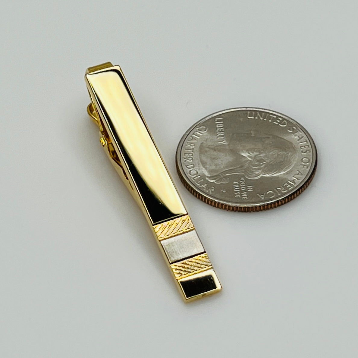 Gold tone tie clip beside quarter for size reference