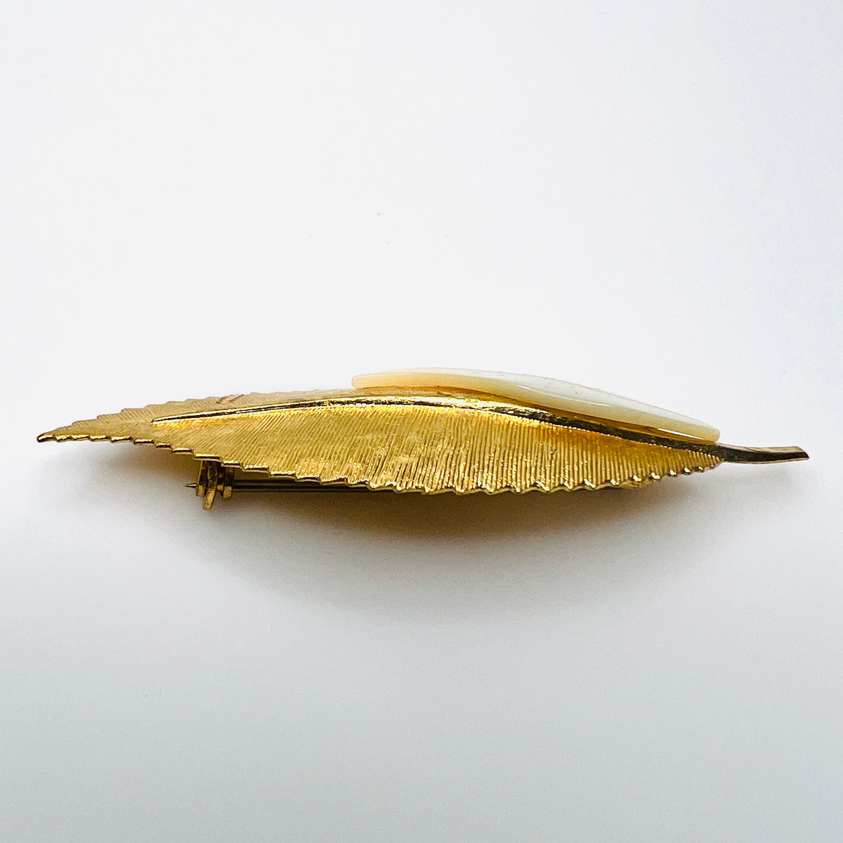 Side view of vintage 1950s gold-tone botanical brooch showing raised mother of pearl leaf and dimensional metal construction.