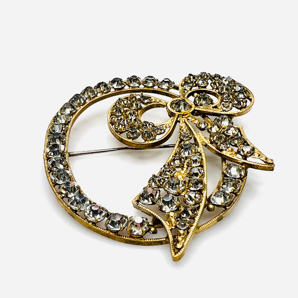 Angled view of the gold-tone bow brooch showing raised prong-set clear crystals and ridged borders.