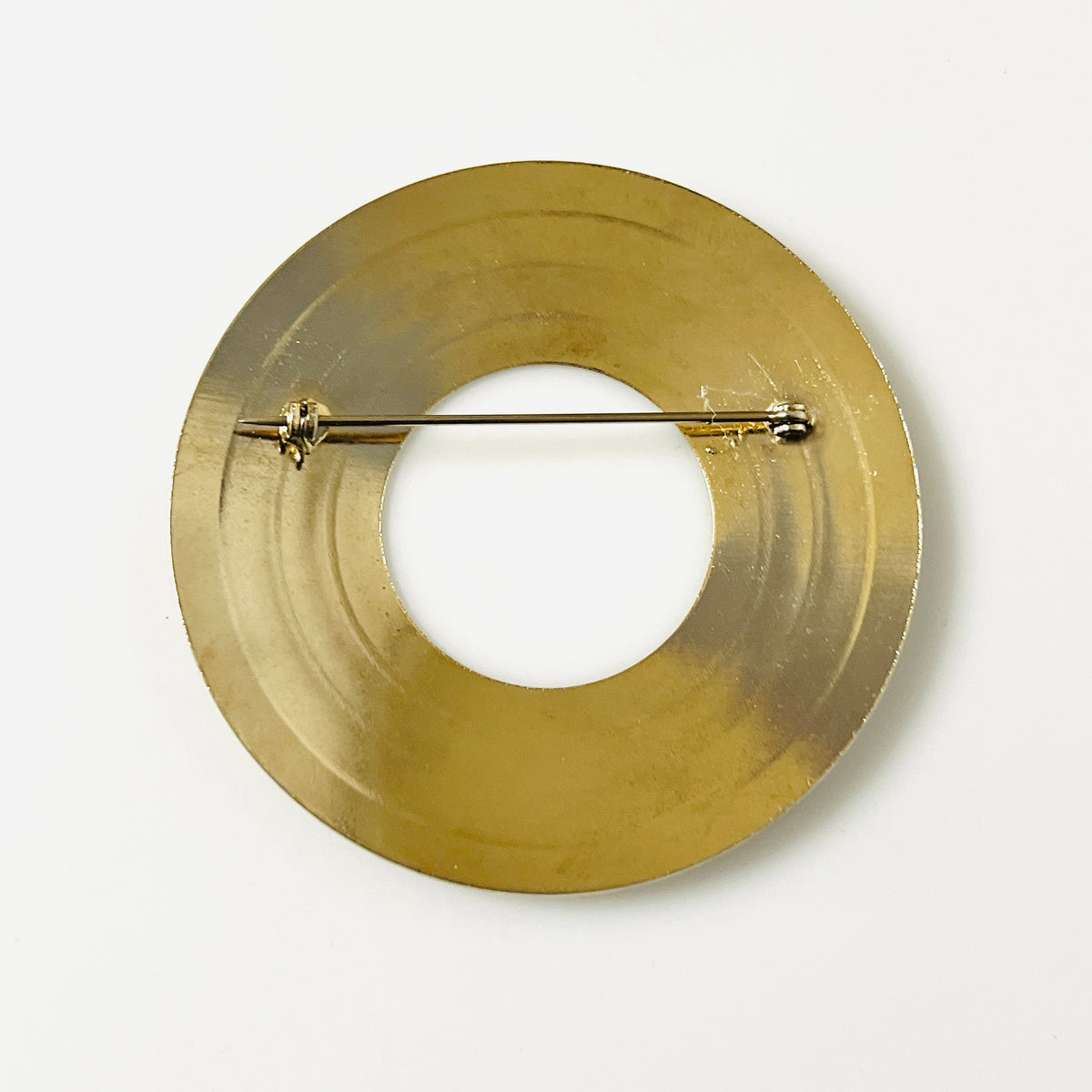 Reverse of unsigned vintage gold tone circle brooch showing pin clasp