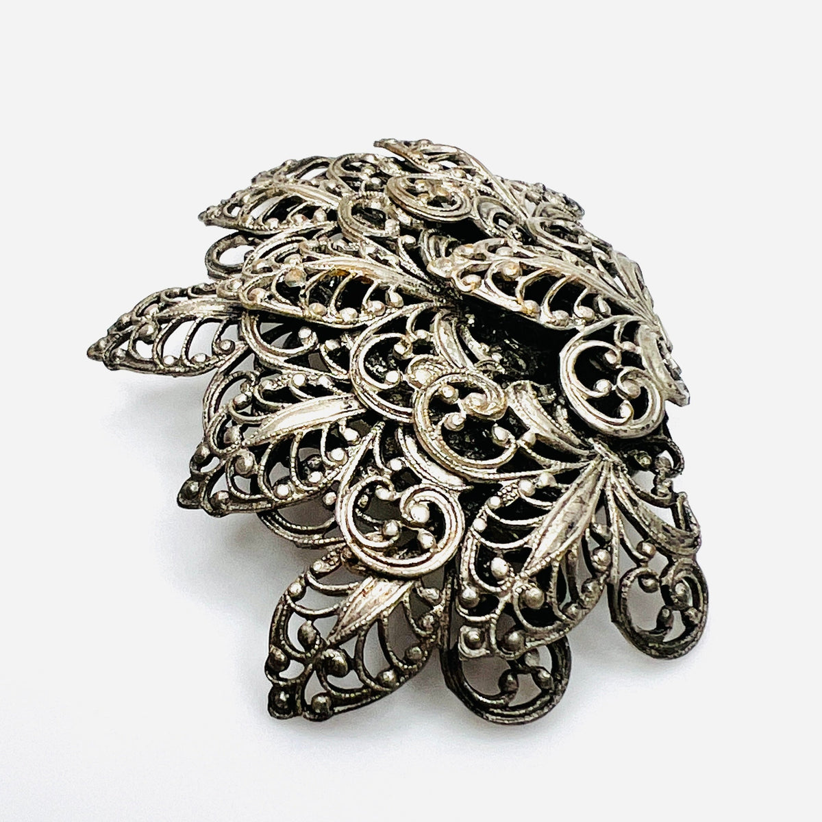 Side view of vintage silver tone filigree brooch showing dimensional layered construction