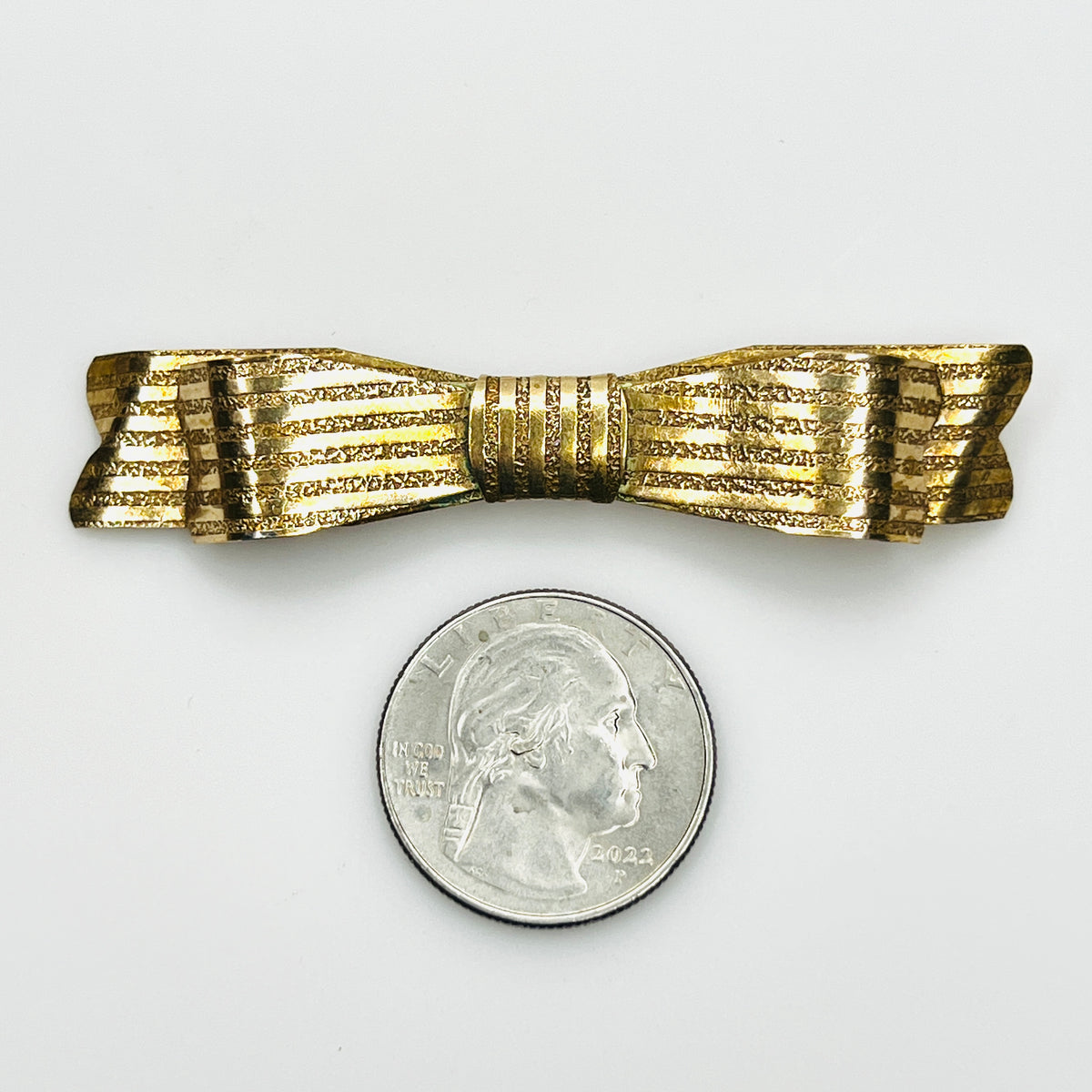Vintage gold-tone ribbon bow brooch beside quarter showing its slender mid-century design and size