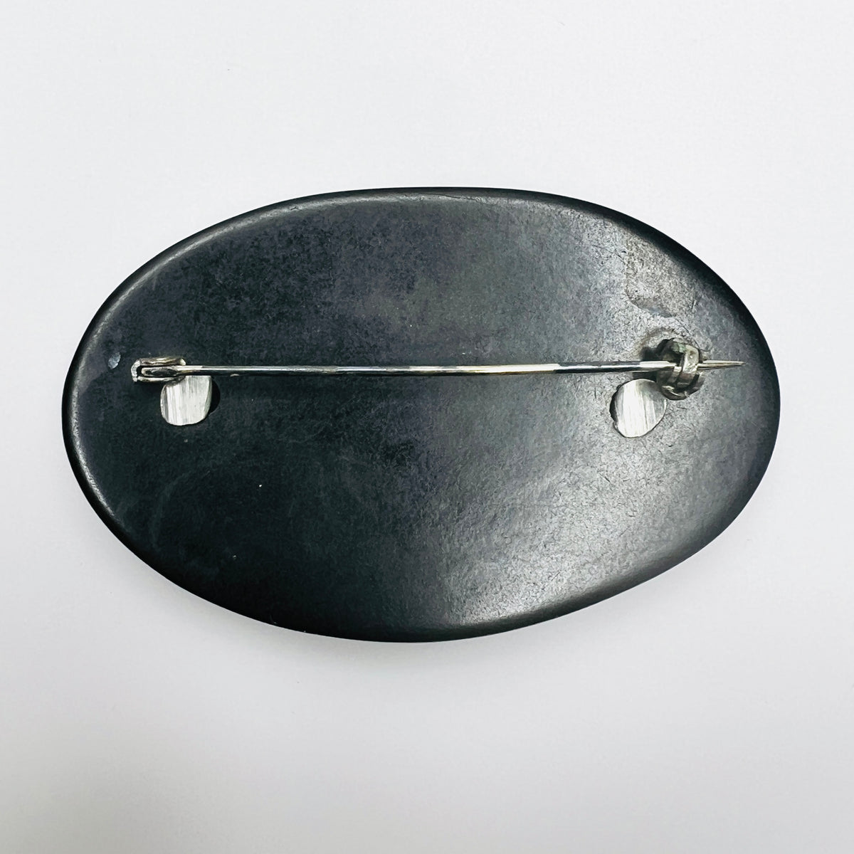 Reverse of vintage oval filigree brooch showing black base, metal attachment posts and rollover clasp