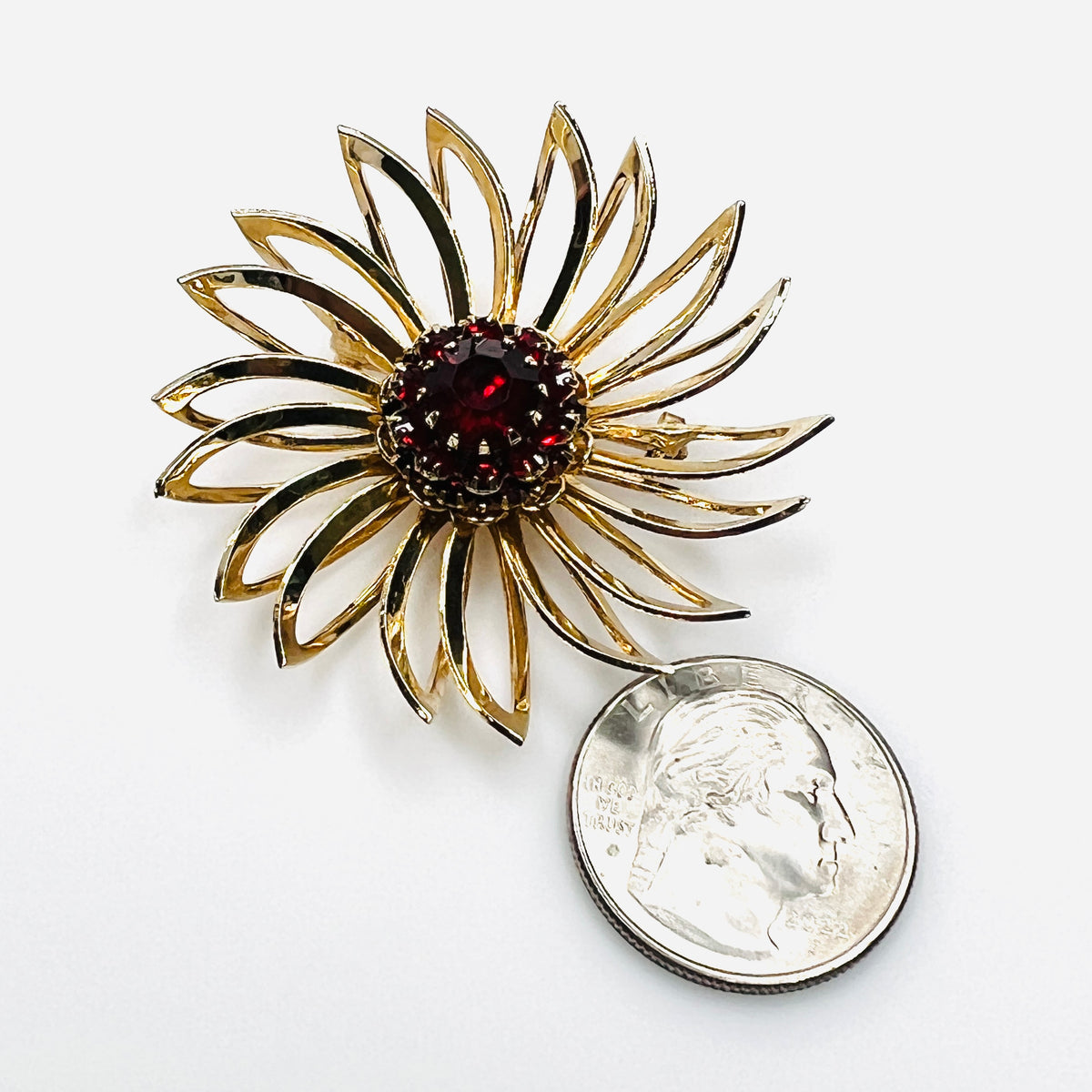 Sarah Coventry ruby red rhinestone flower brooch shown beside quarter for scale