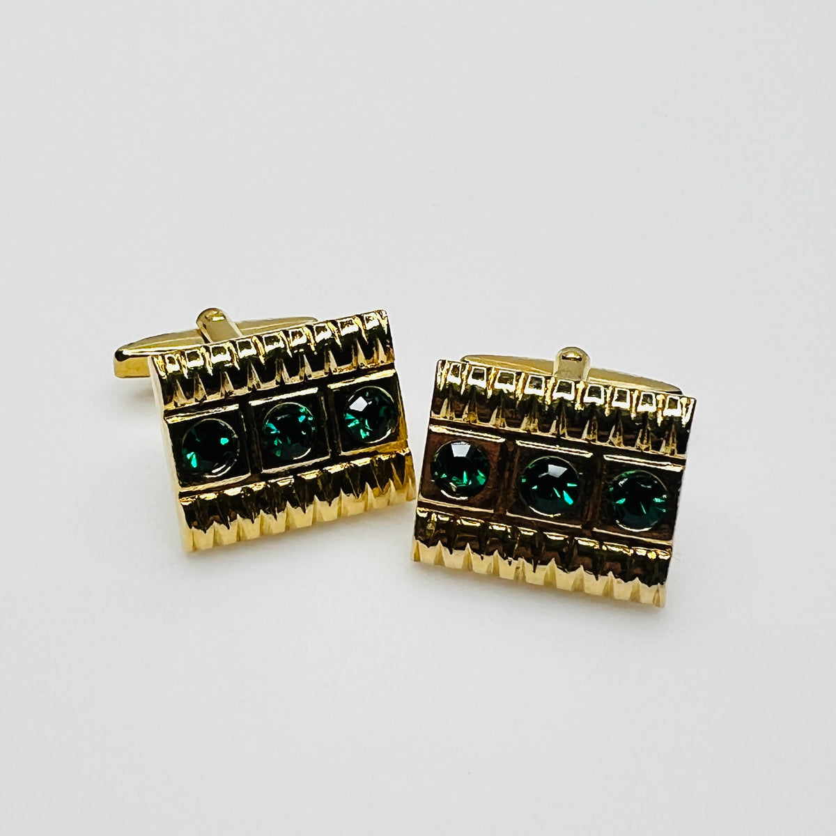Close-up of gold tone West German cufflinks with three emerald green rhinestones and geometric detailing