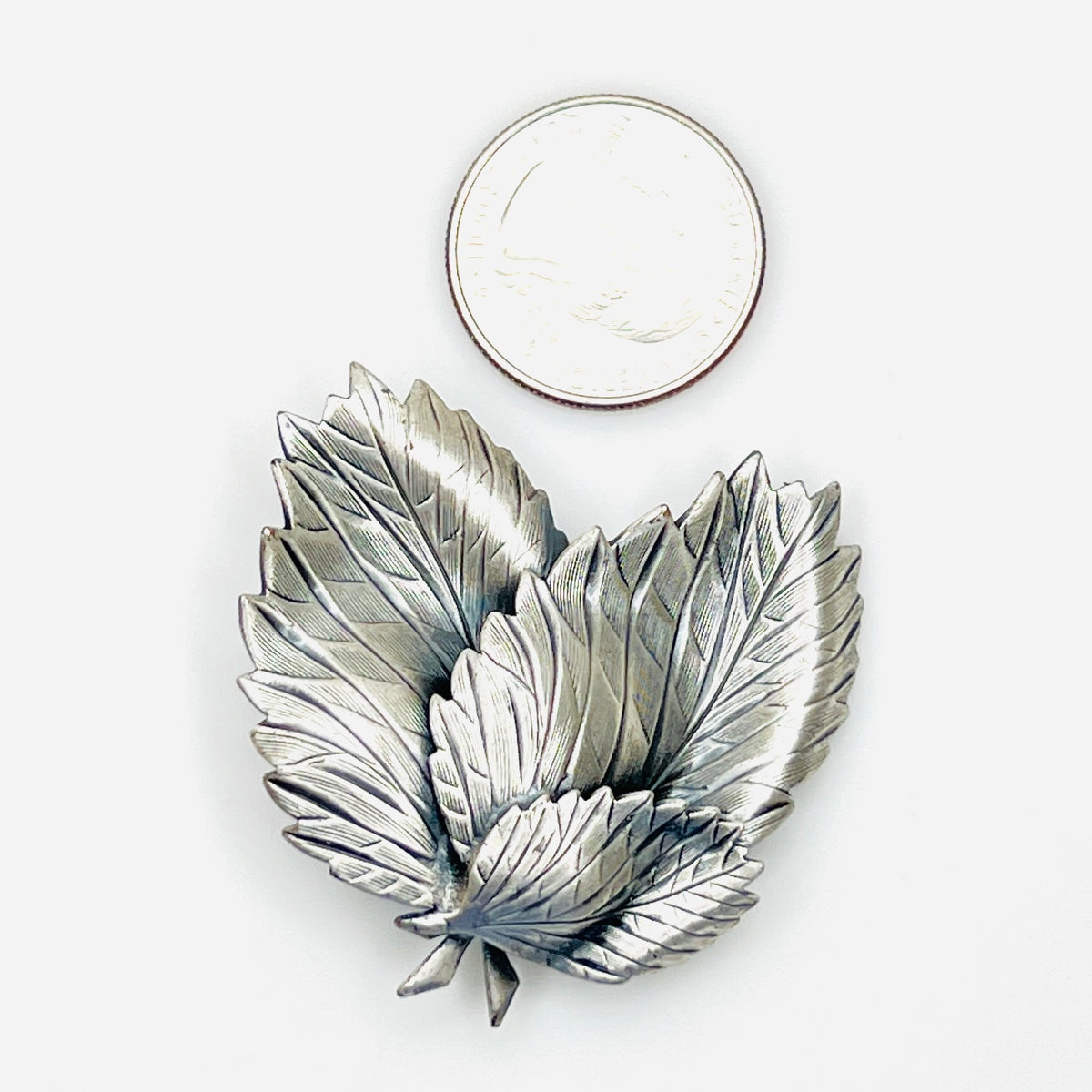 Silver tone layered leaf brooch shown beside quarter for scale