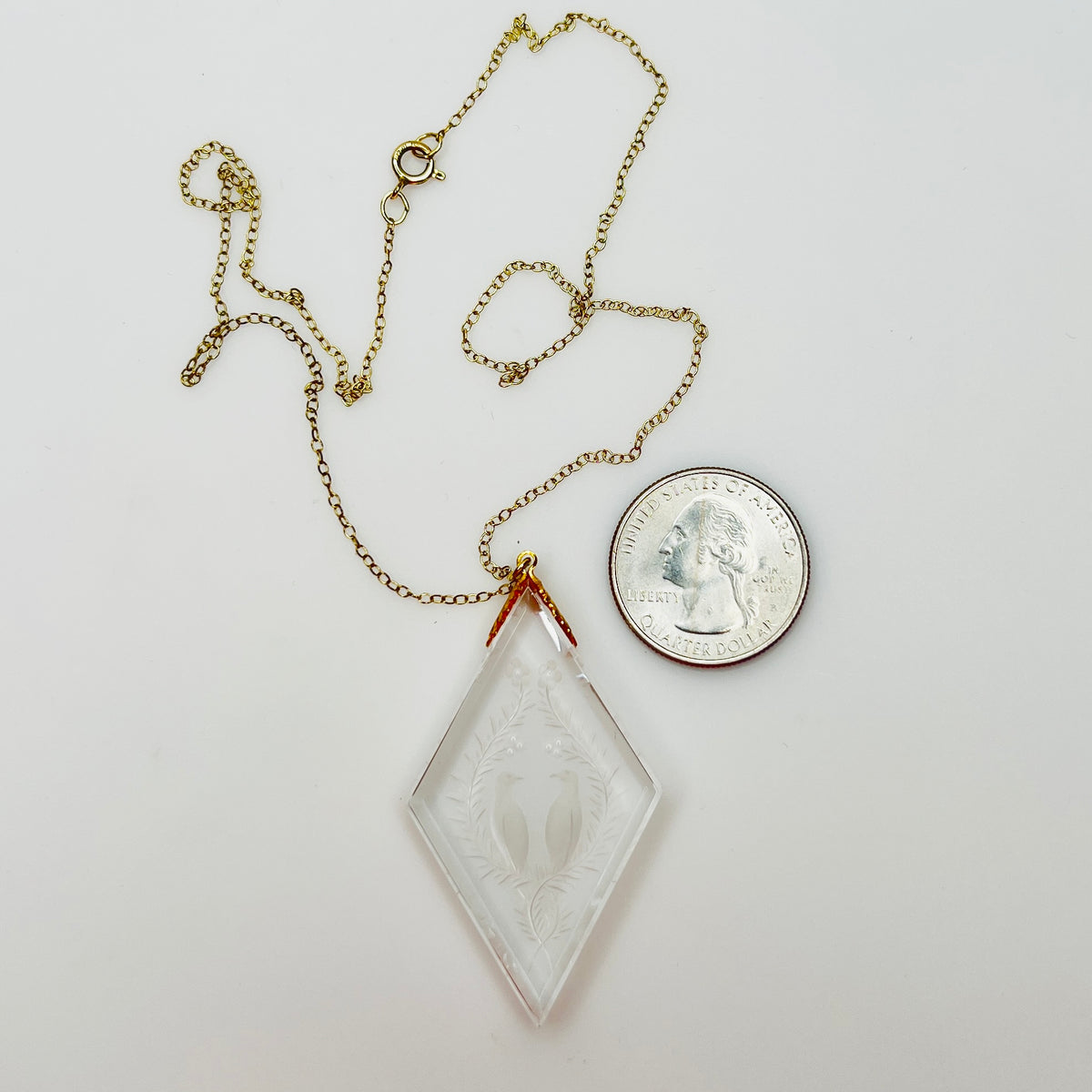 Close-up of crystal love birds pendant next to coin for scale