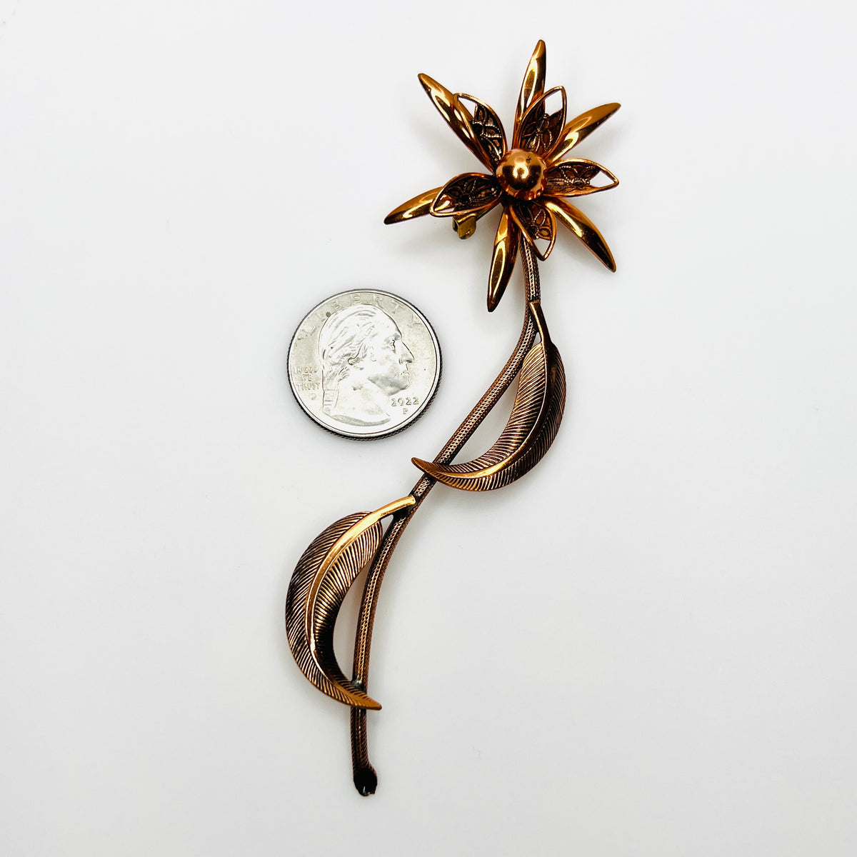 Long-stem copper floral brooch beside quarter showing scale and dimensional flower design