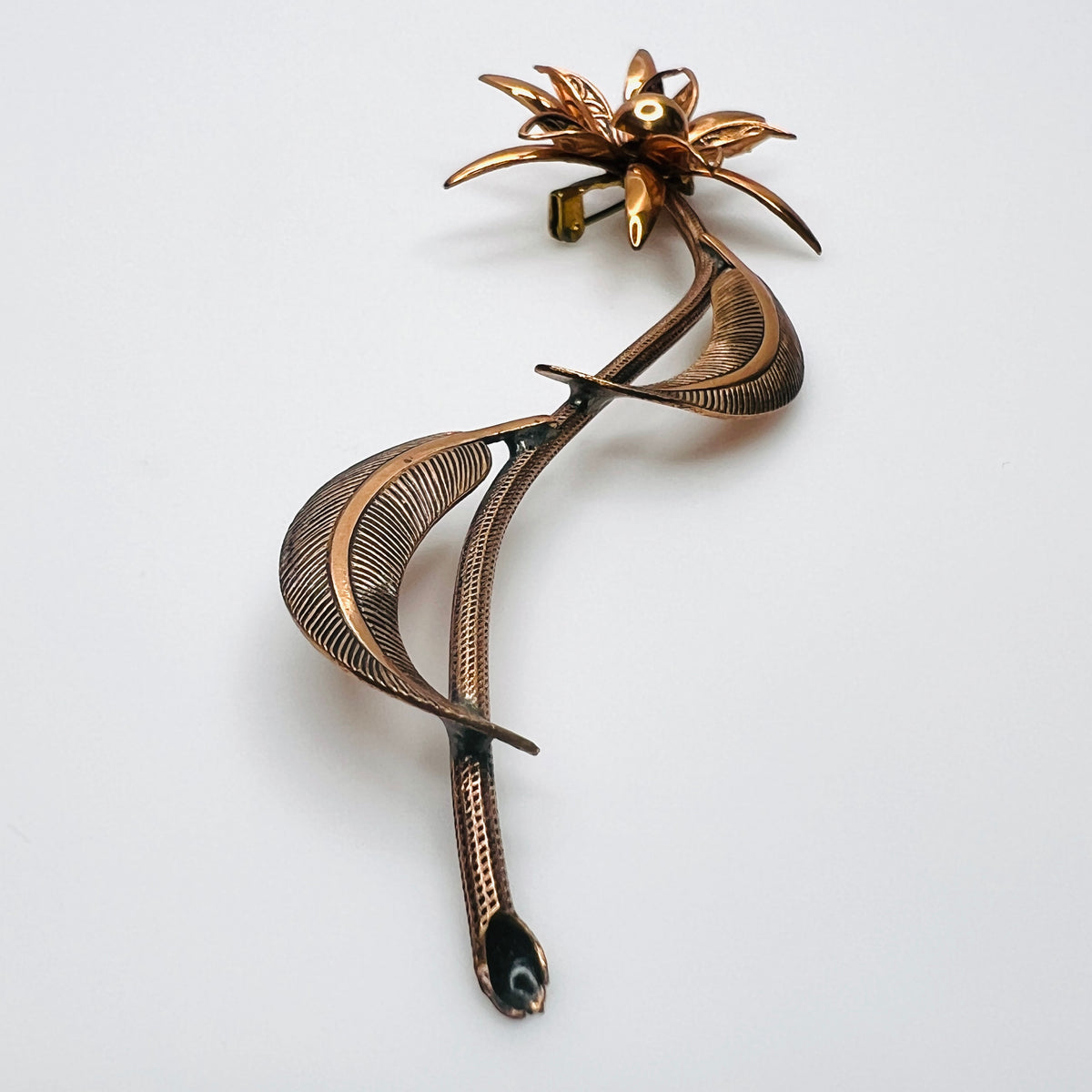 Side profile of vintage copper flower brooch showing raised petals and sculptural curved leaves