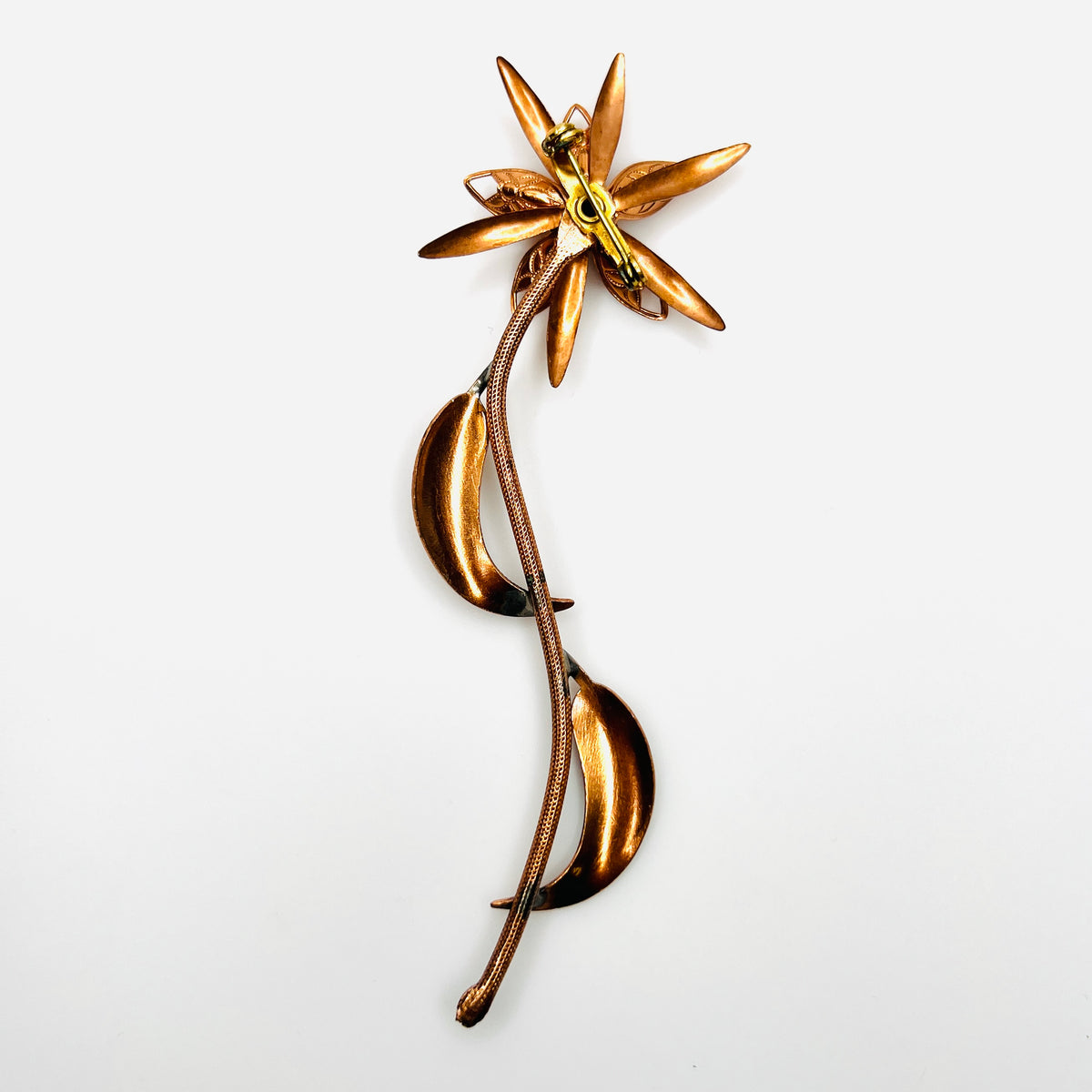 Reverse of 1970s copper-tone flower brooch showing long stem, metal construction and rollover clasp