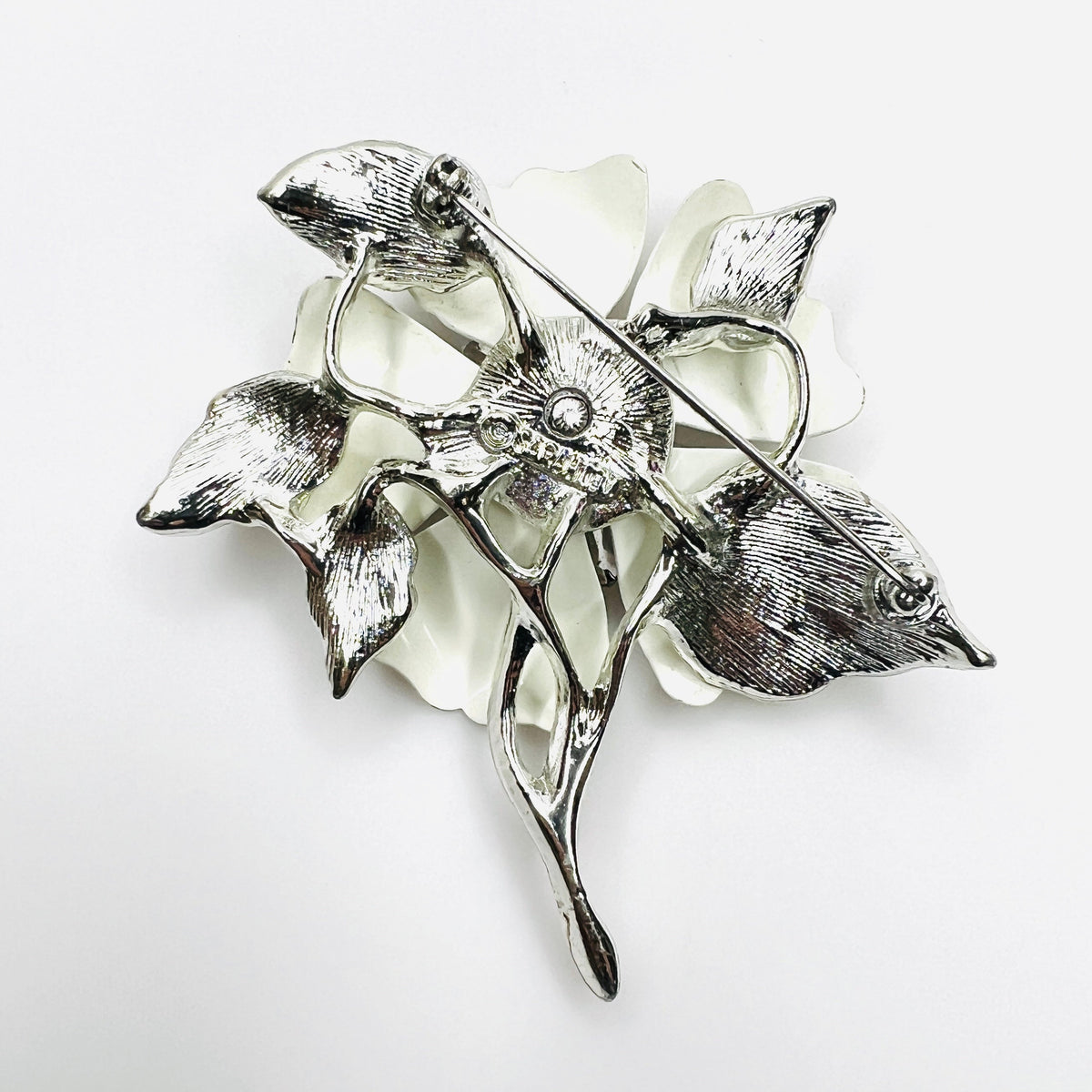 Reverse of signed Sarah Coventry white enamel flower brooch with silver-tone pin closure