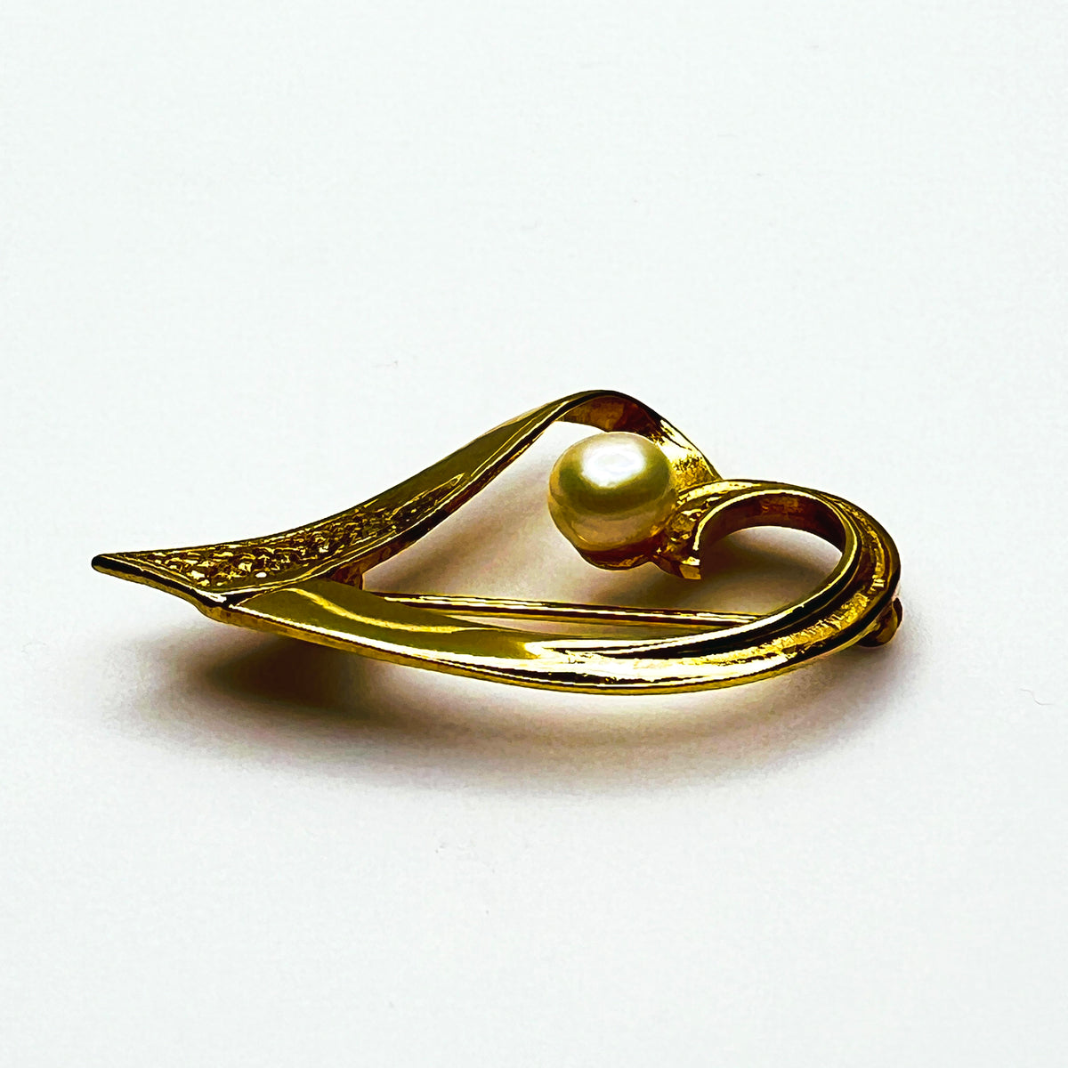 Side view of vintage sterling silver vermeil heart pin showing dimensional ribbon construction, textured detailing and raised pearl.