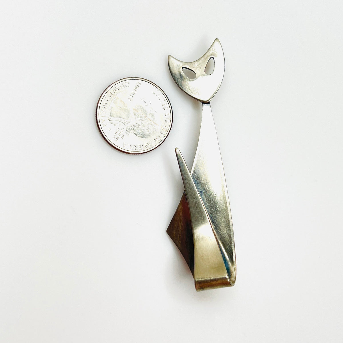 Artisan stainless steel cat brooch beside quarter showing size and sleek Modernist silhouette.