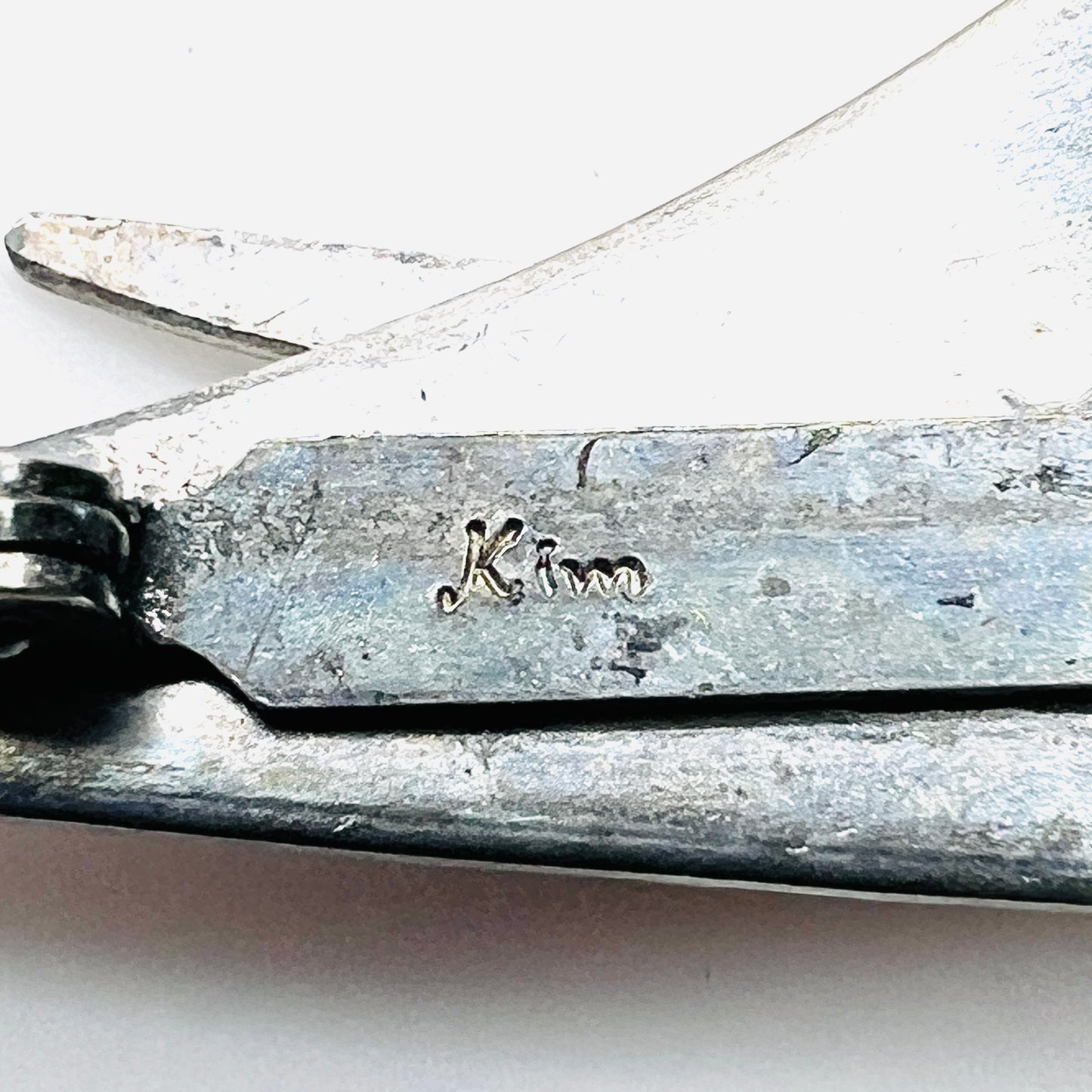 Close-up of Kim signature on vintage artisan stainless steel cat brooch.