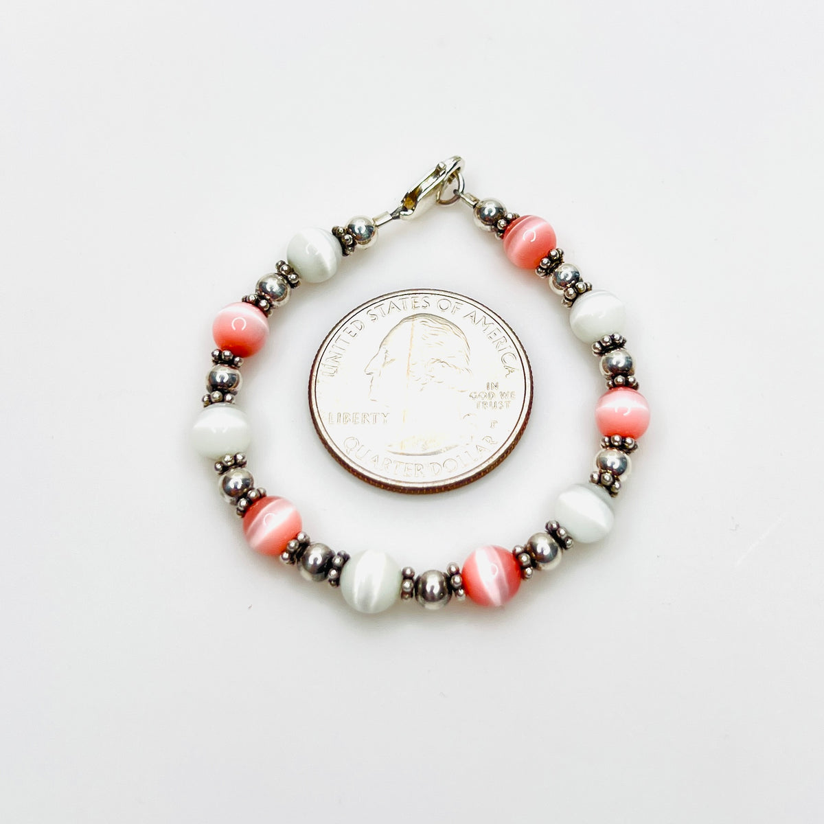 Pink and white cat's eye bracelet shown with quarter for scale