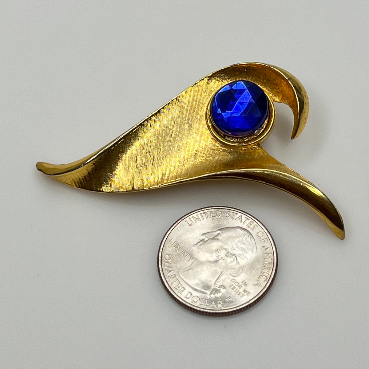 Modernist gold-tone brooch with sculptural wave shape and cobalt blue rhinestone center
