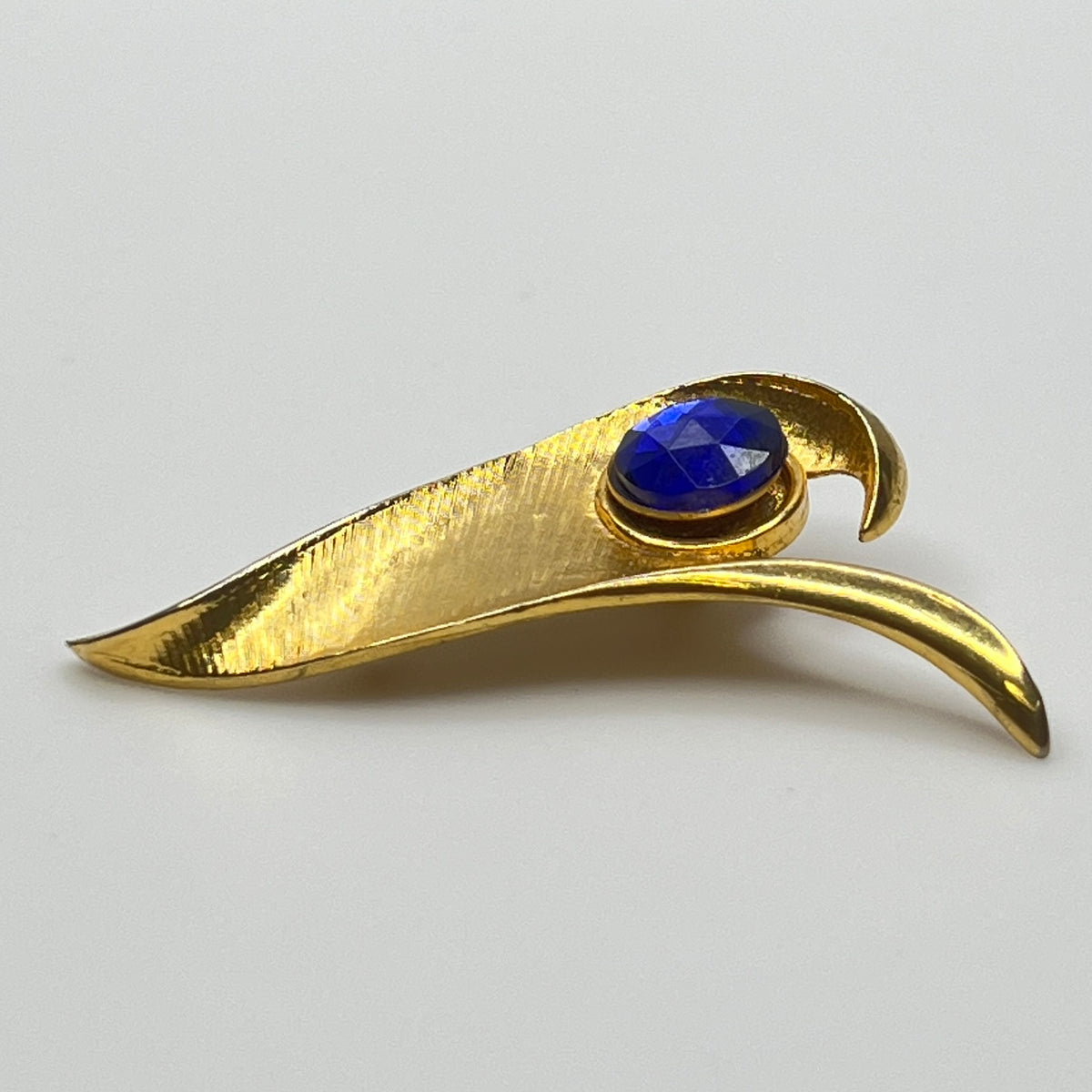 Modernist gold-tone brooch with sculptural wave shape and cobalt blue rhinestone center