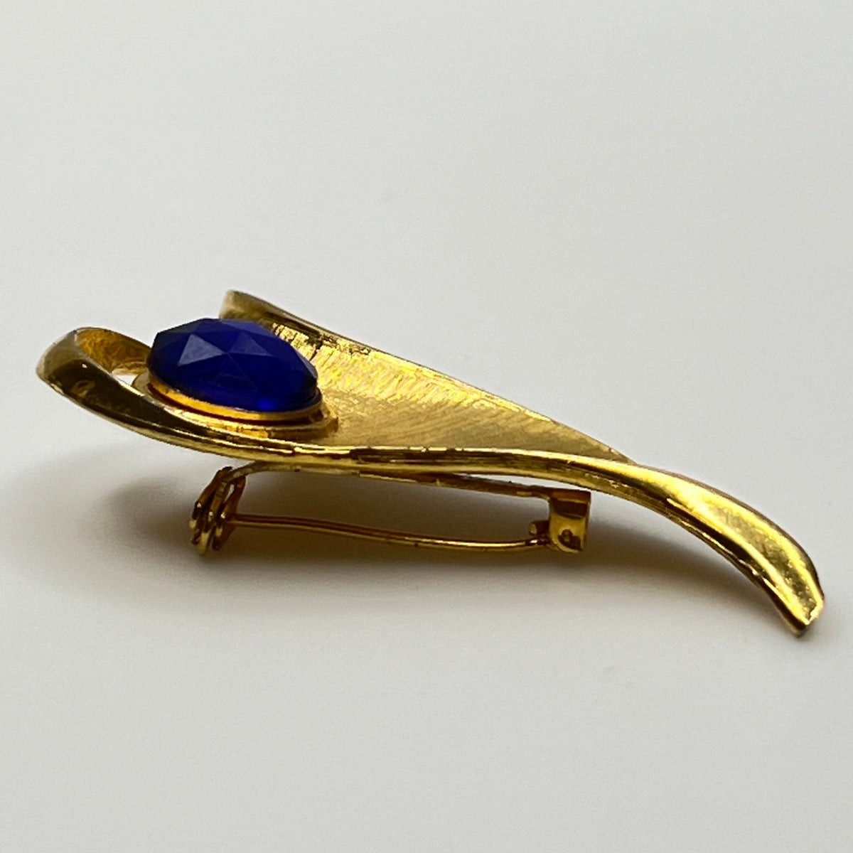 Modernist gold-tone brooch with sculptural wave shape and cobalt blue rhinestone center