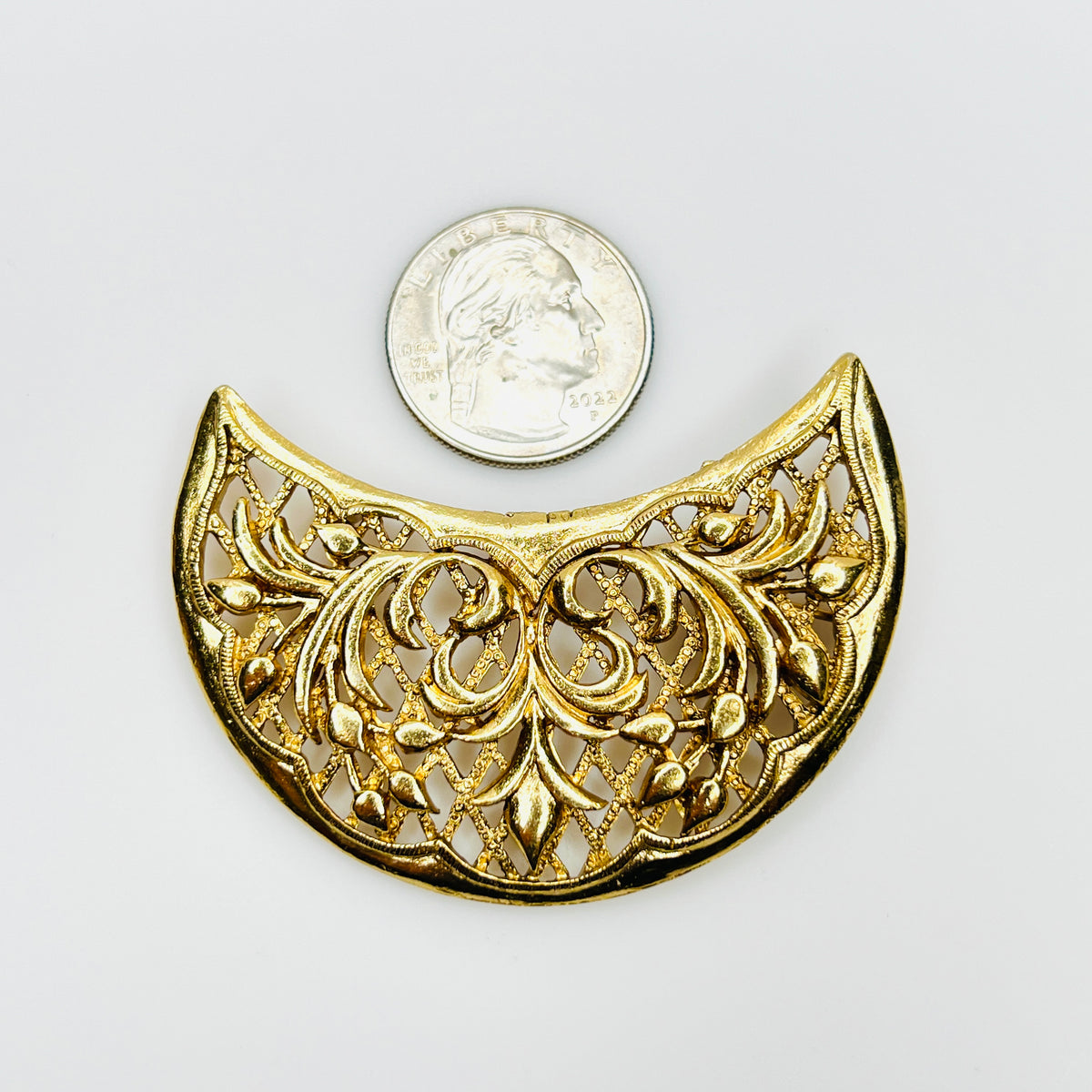 Signed Lisner gold-tone floral crescent brooch beside a quarter showing its generous size and symmetrical botanical design.