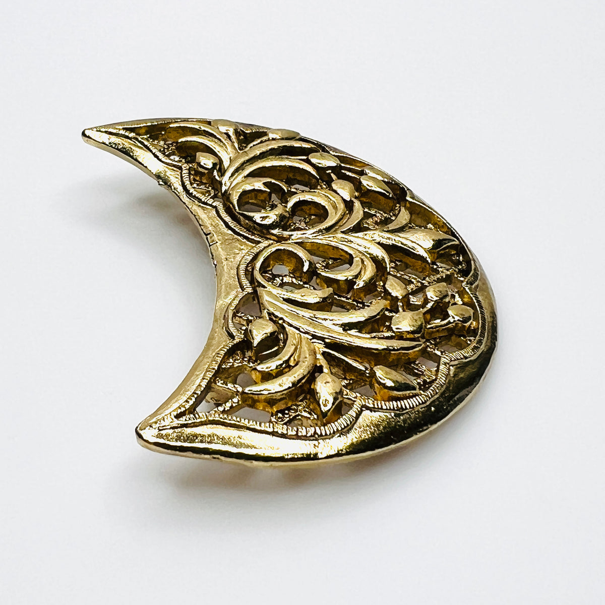 Angled view of vintage Lisner crescent brooch showing dimensional gold-tone scrollwork and textured openwork lattice.