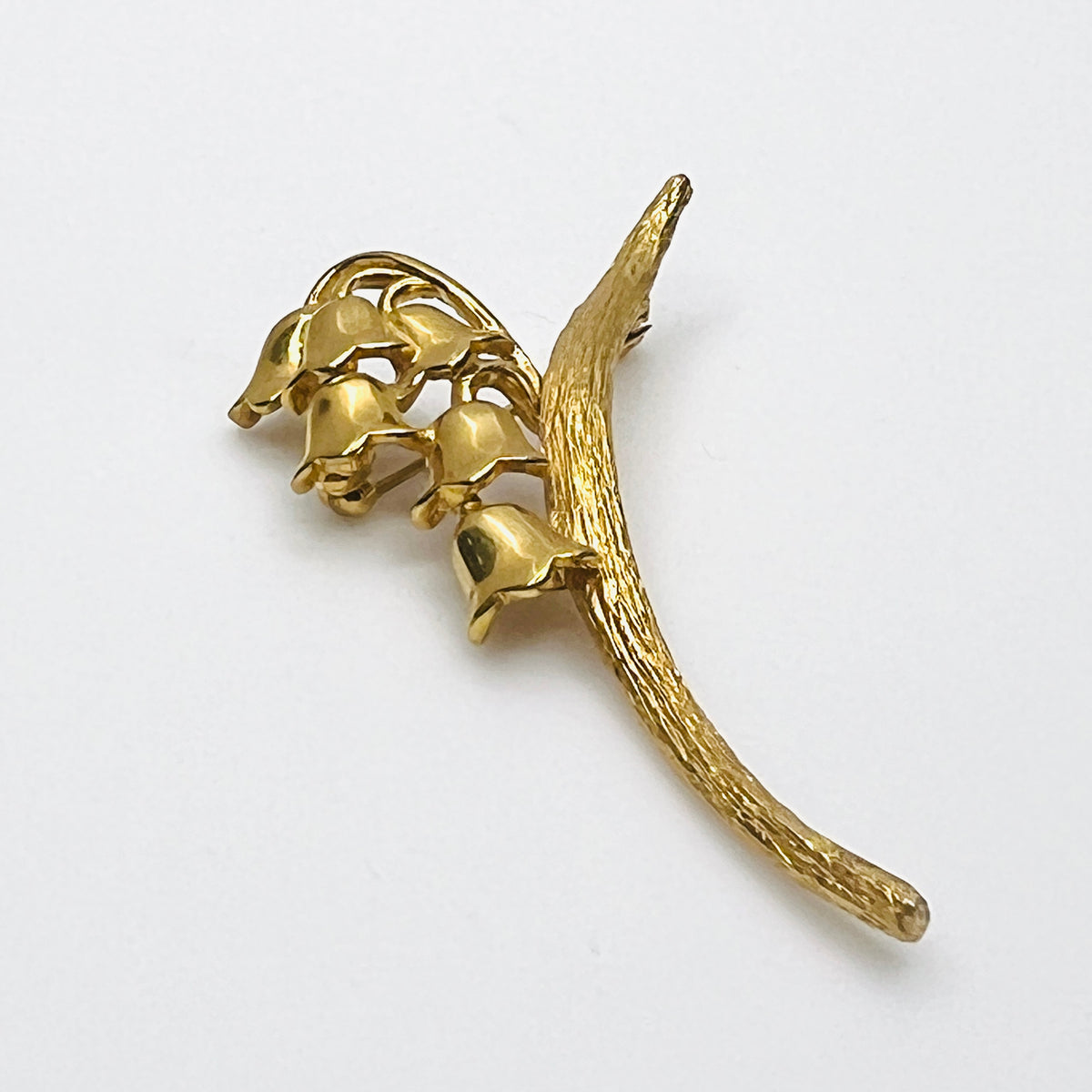 Side view of vintage gold-tone Monet flower brooch showing dimensional bell blossoms and textured stem