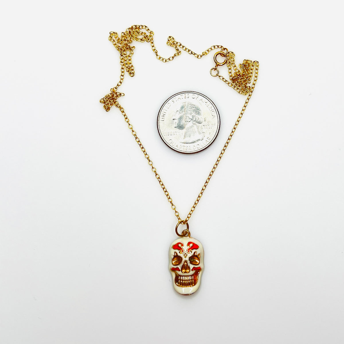 Enamel sugar skull pendant necklace beside quarter showing size and 20-inch chain.
