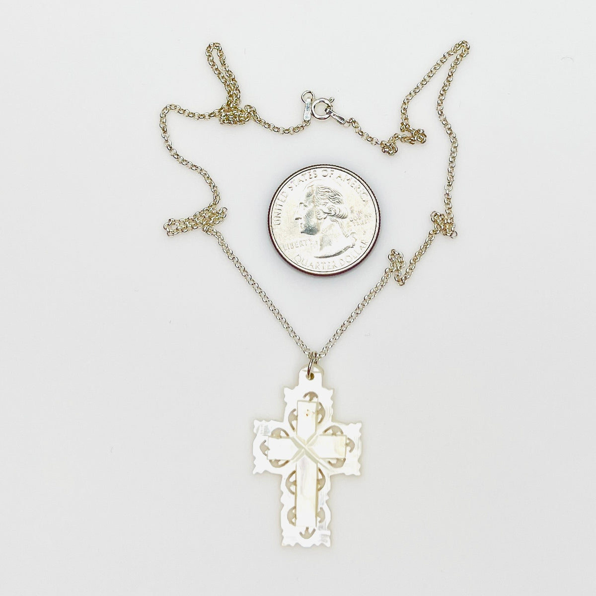 Hand-carved Mother of Pearl Bethlehem cross necklace with quarter for size comparison.